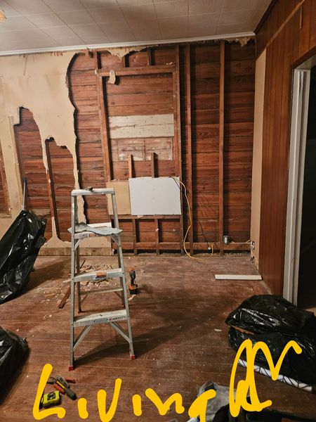 Interior room under renovation; exposed wooden walls, ladder, debris, and trash bags.