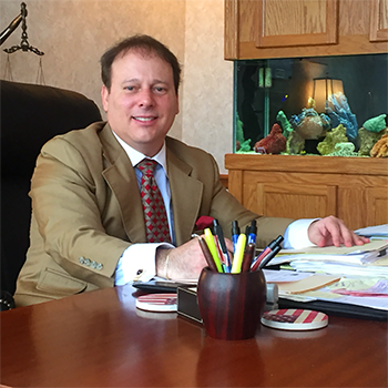 A man in a suit and tie is sitting at a desk in front of an aquarium