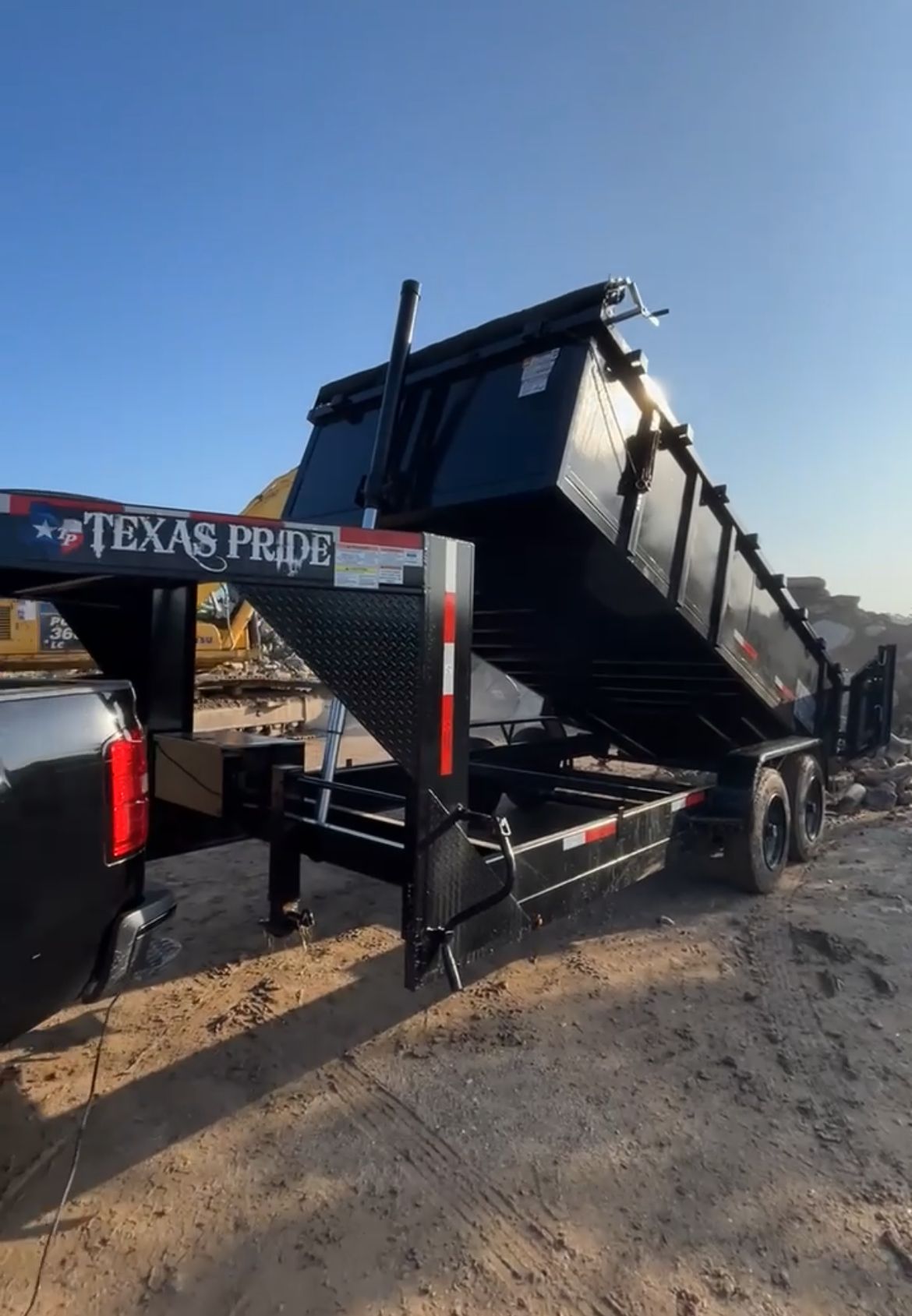 A dump trailer is parked next to a truck on a dirt road.