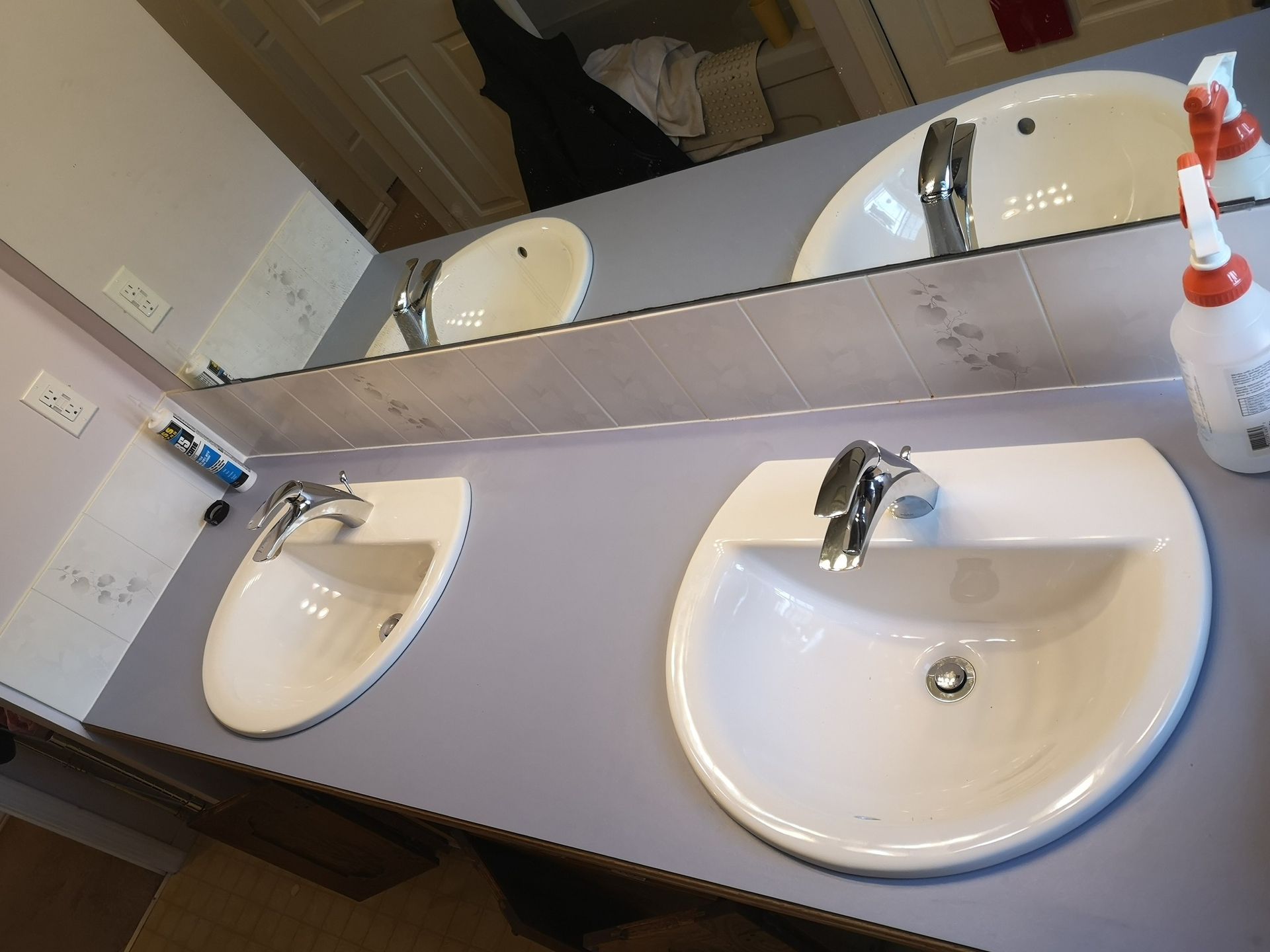 A double bathroom vanity with two white oval sinks, chrome faucets, and a soap dispenser on a gray countertop.