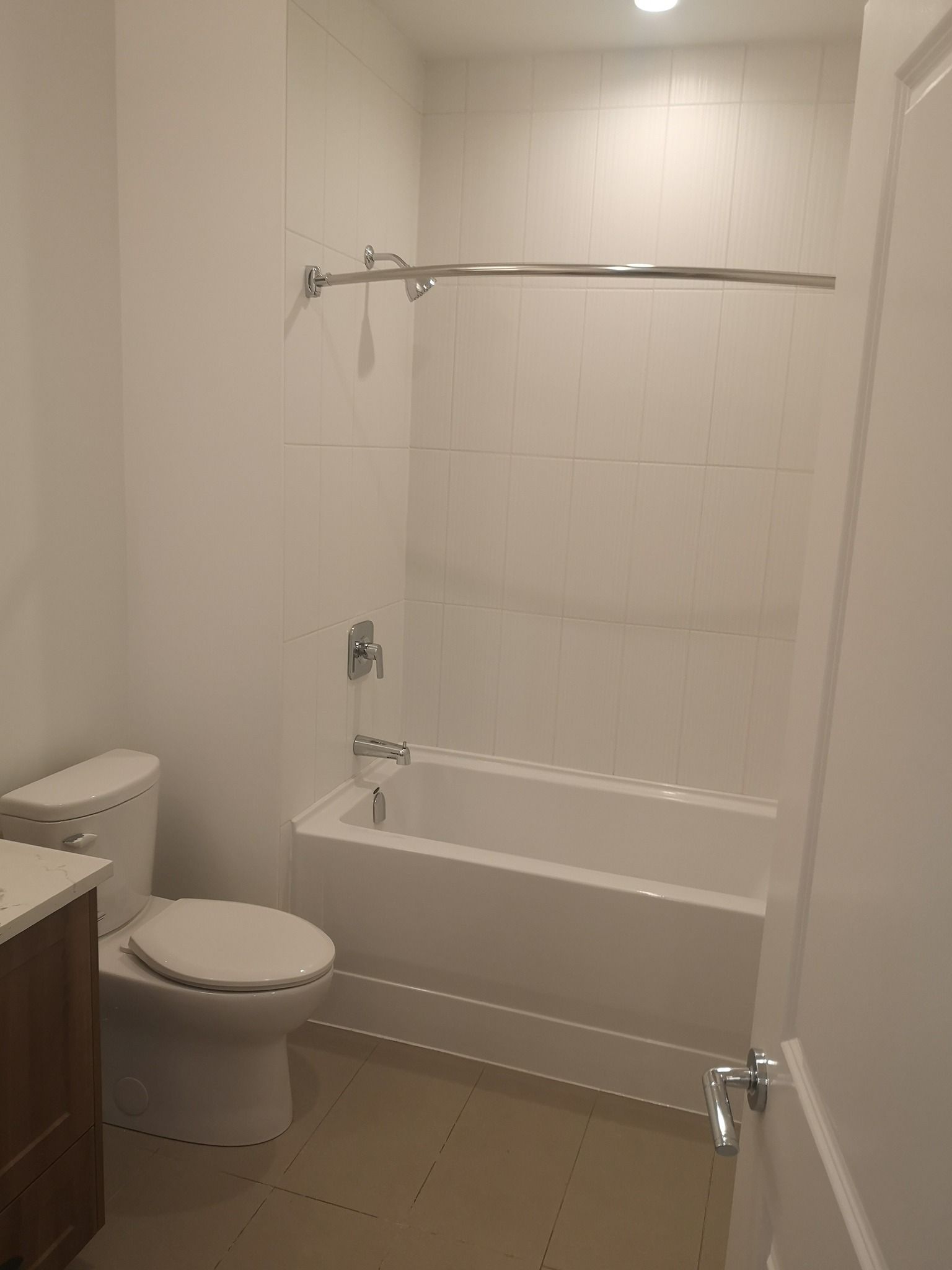 A neutral-toned bathroom featuring a white toilet, a bathtub with a shower head, and a curved shower curtain rod.