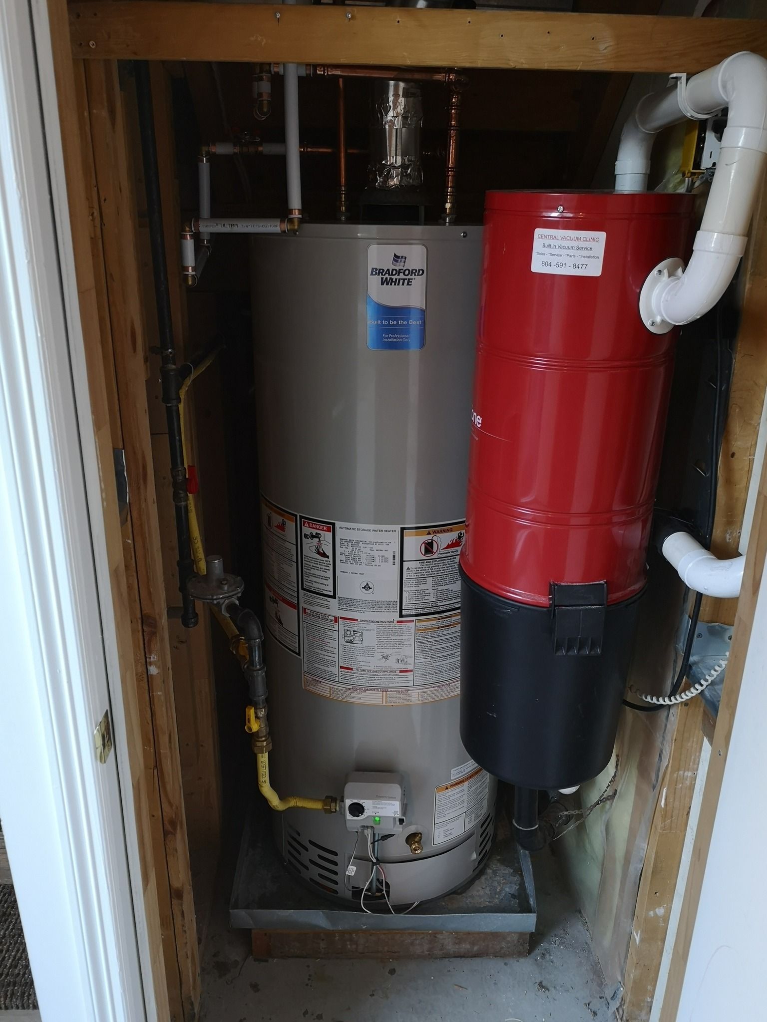 A tall grey water heater and a red cylindrical vacuum unit installed in a closet enclosure.