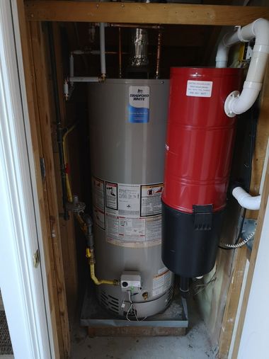 A tall grey water heater and a red cylindrical vacuum unit installed in a closet enclosure.