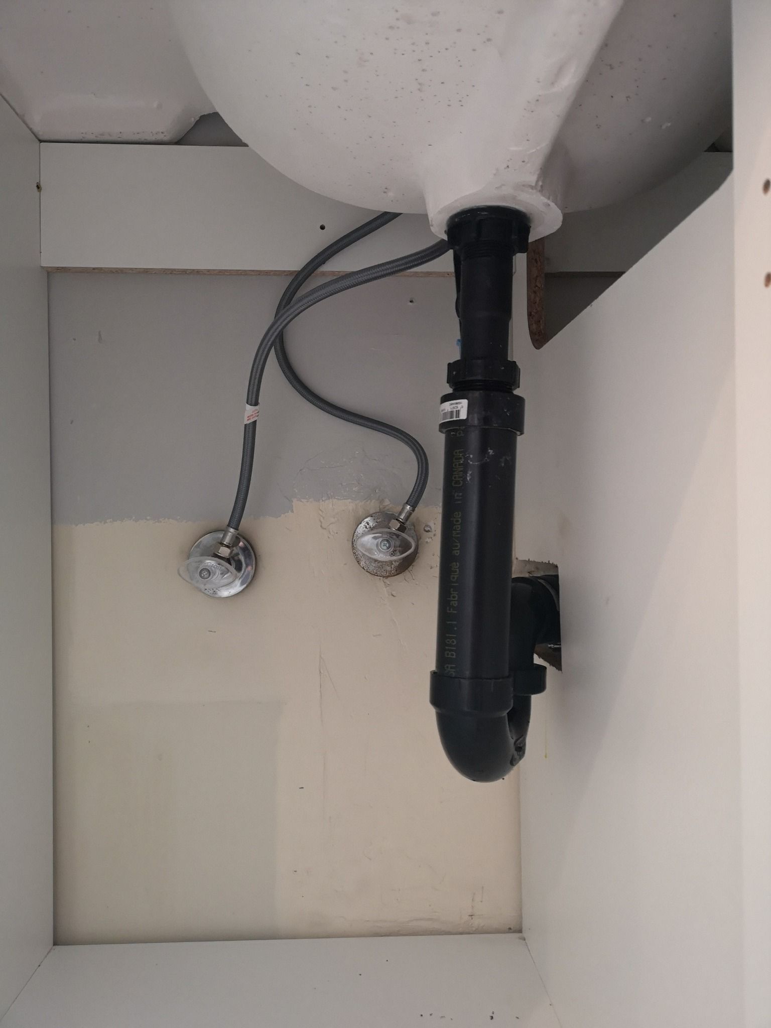 The underside of a sink cabinet showing water supply lines connected to valves and a black P-trap drain pipe.