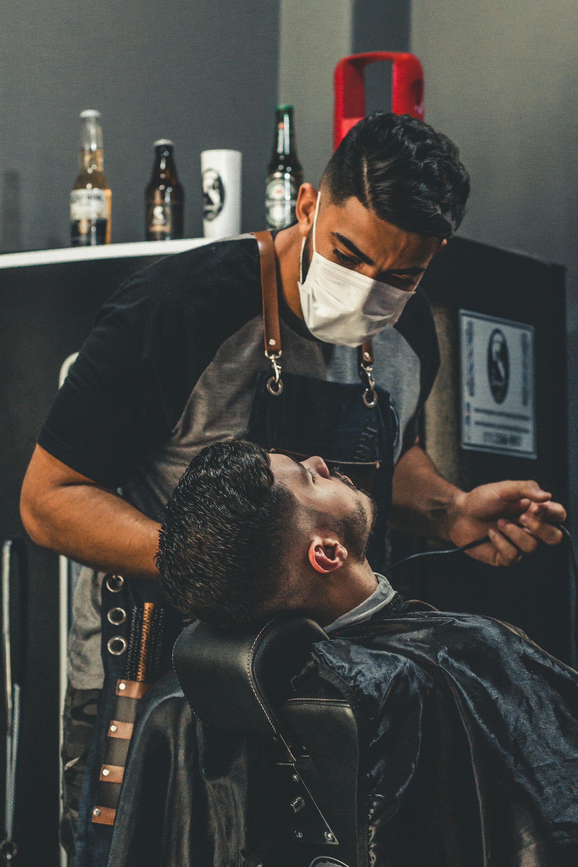 A man is getting his hair cut by a barber wearing a mask.