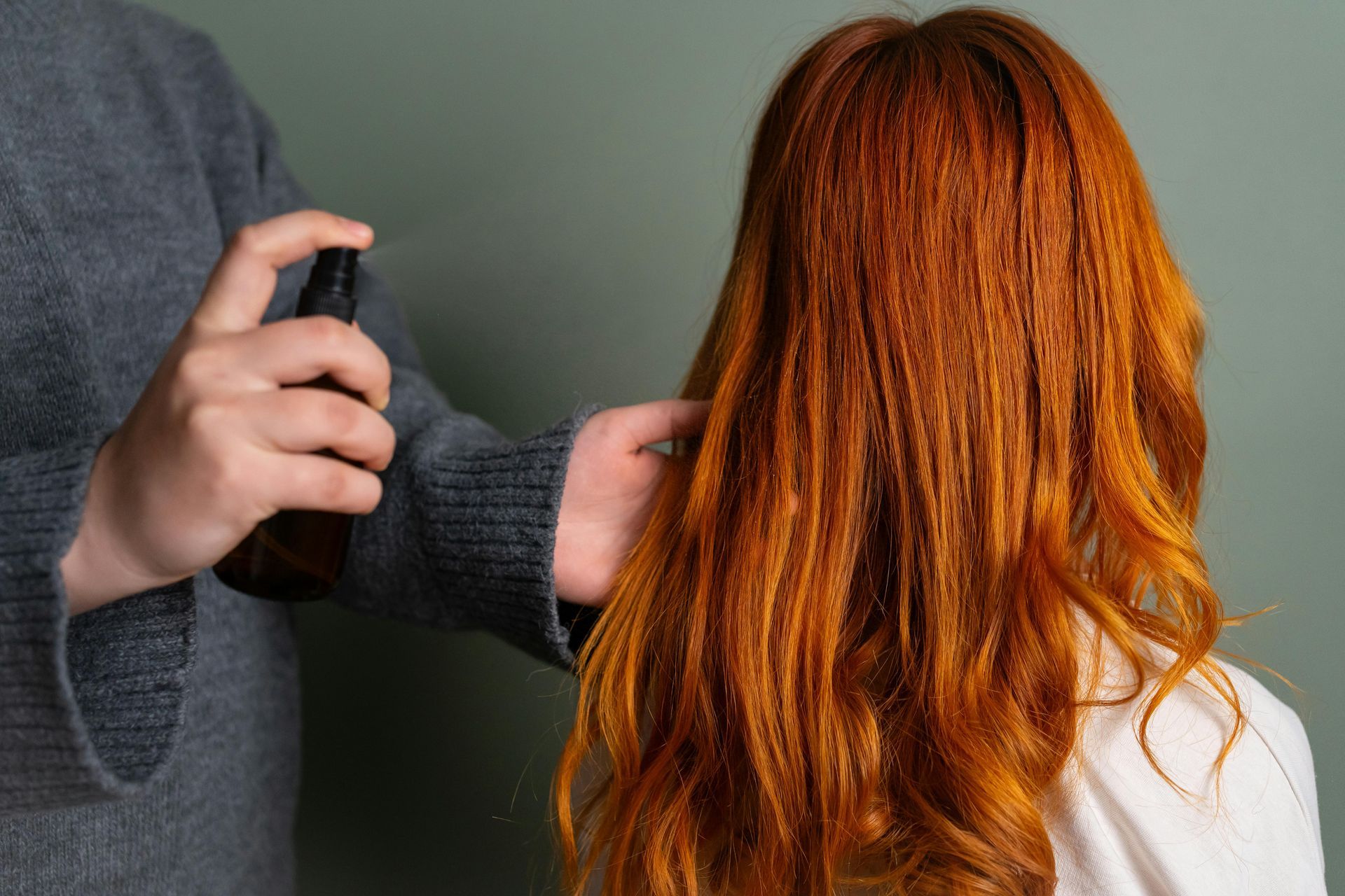 A man is spraying a woman 's hair with a spray bottle.