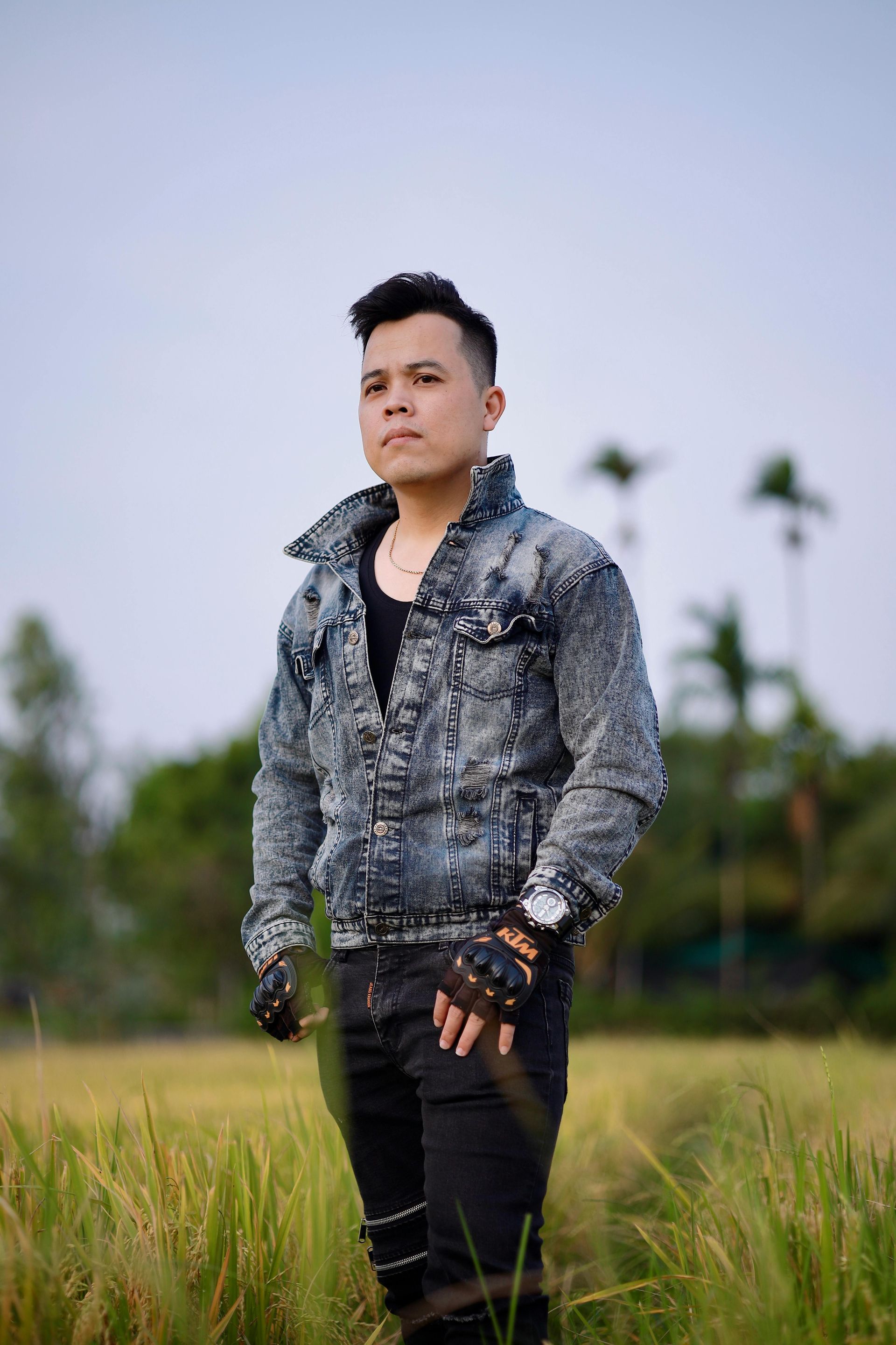 A man in a denim jacket is standing in a field of tall grass.