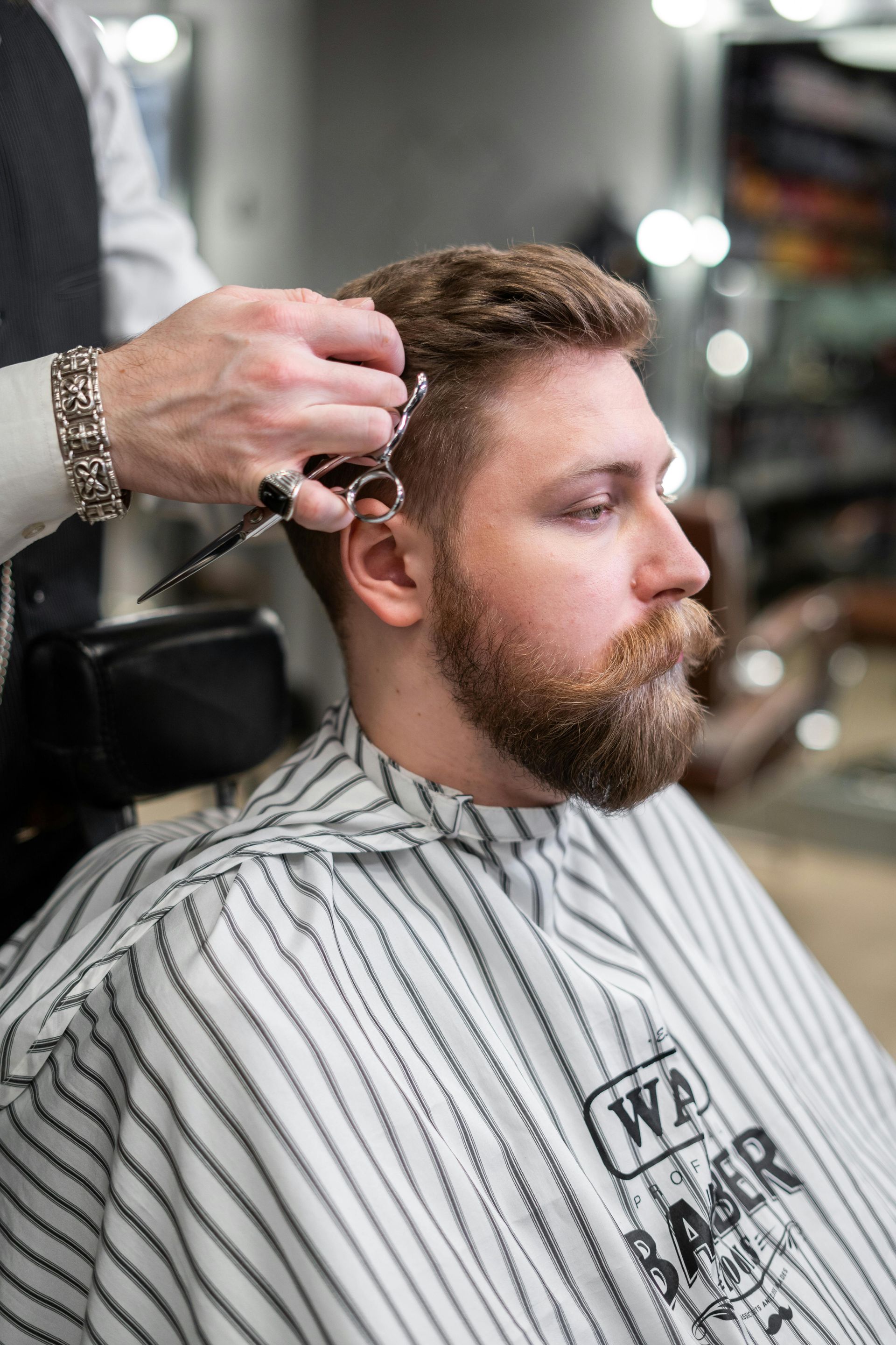 A man with a beard is getting his hair cut by a barber in a barber shop.
