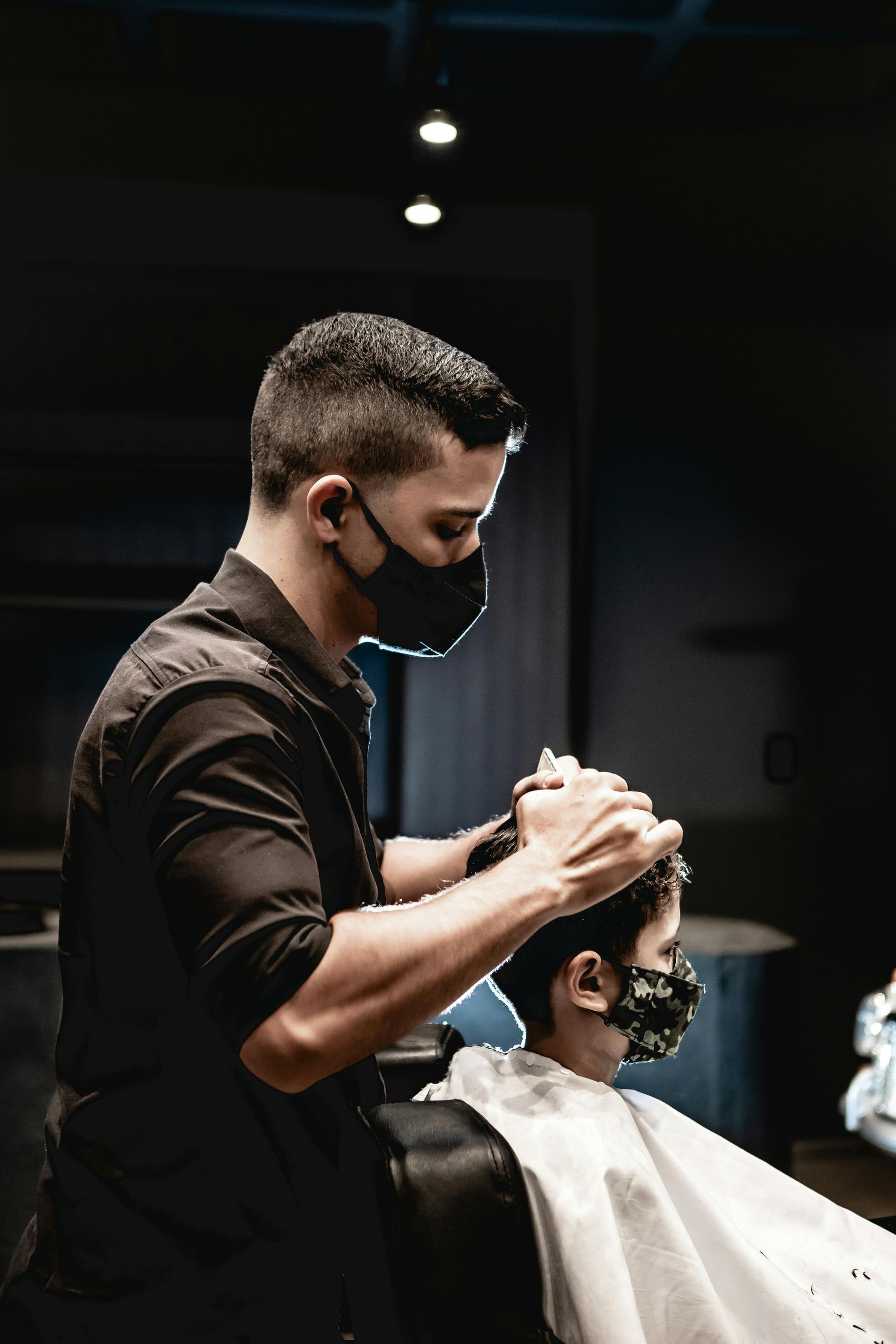 A man wearing a mask is getting his hair cut by a barber.