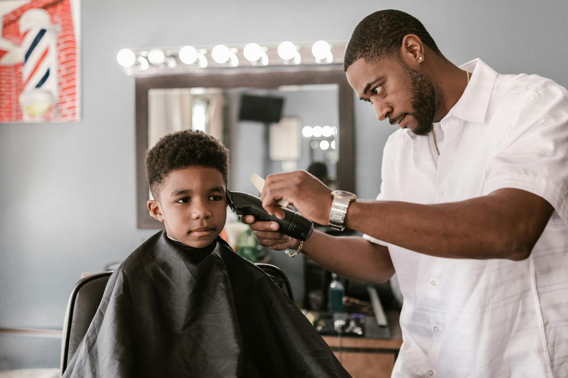 A young boy is getting his hair cut by a barber in a barber shop.