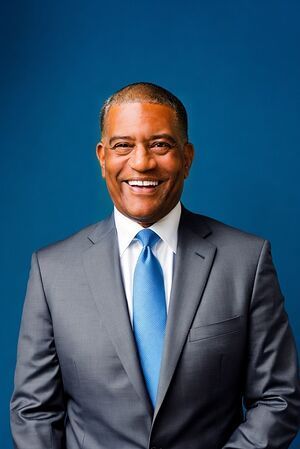 A man in a suit and tie is smiling in front of a blue background.