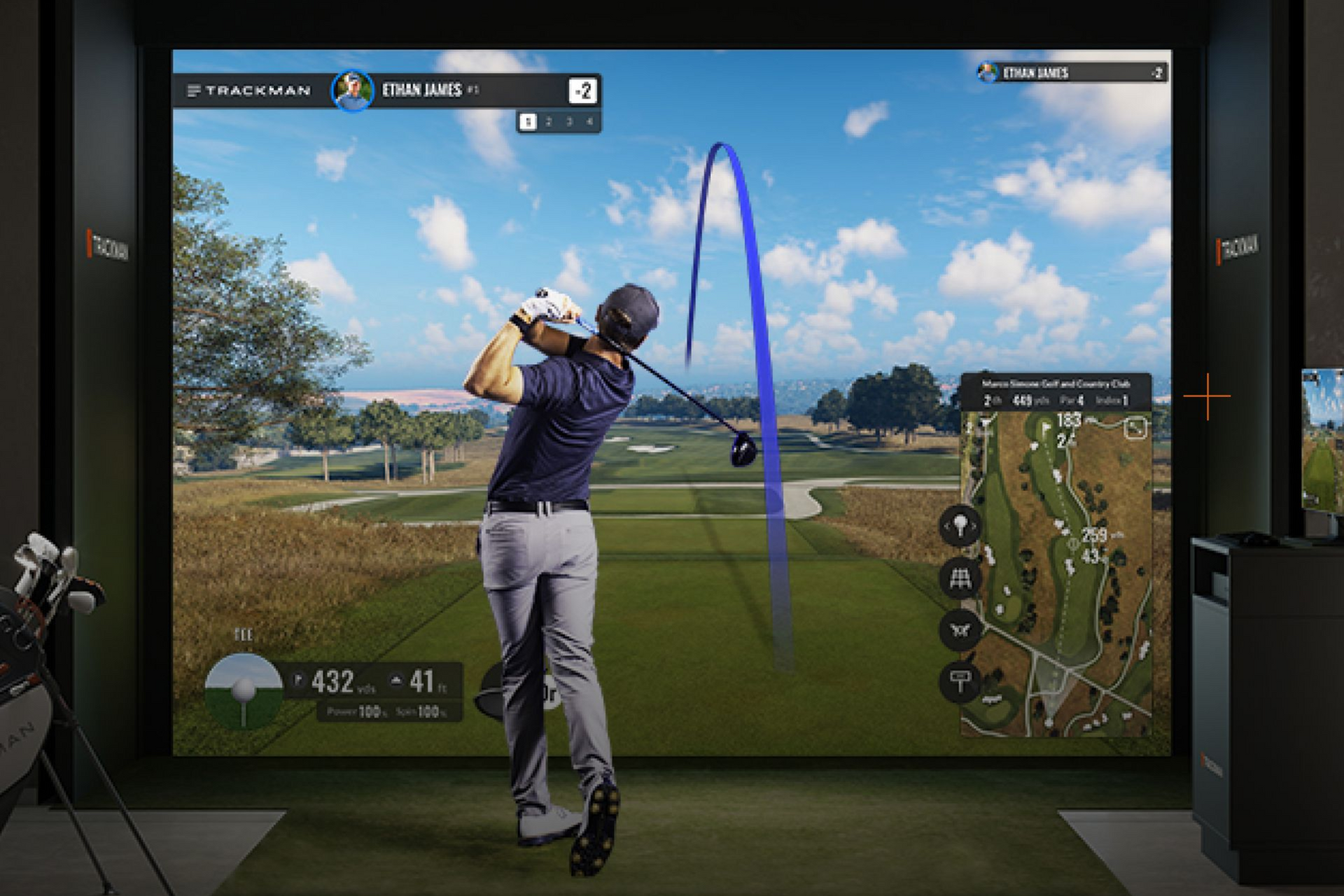 Golfer swinging a club in a golf simulator, blue ball flight displayed on screen, green grass.