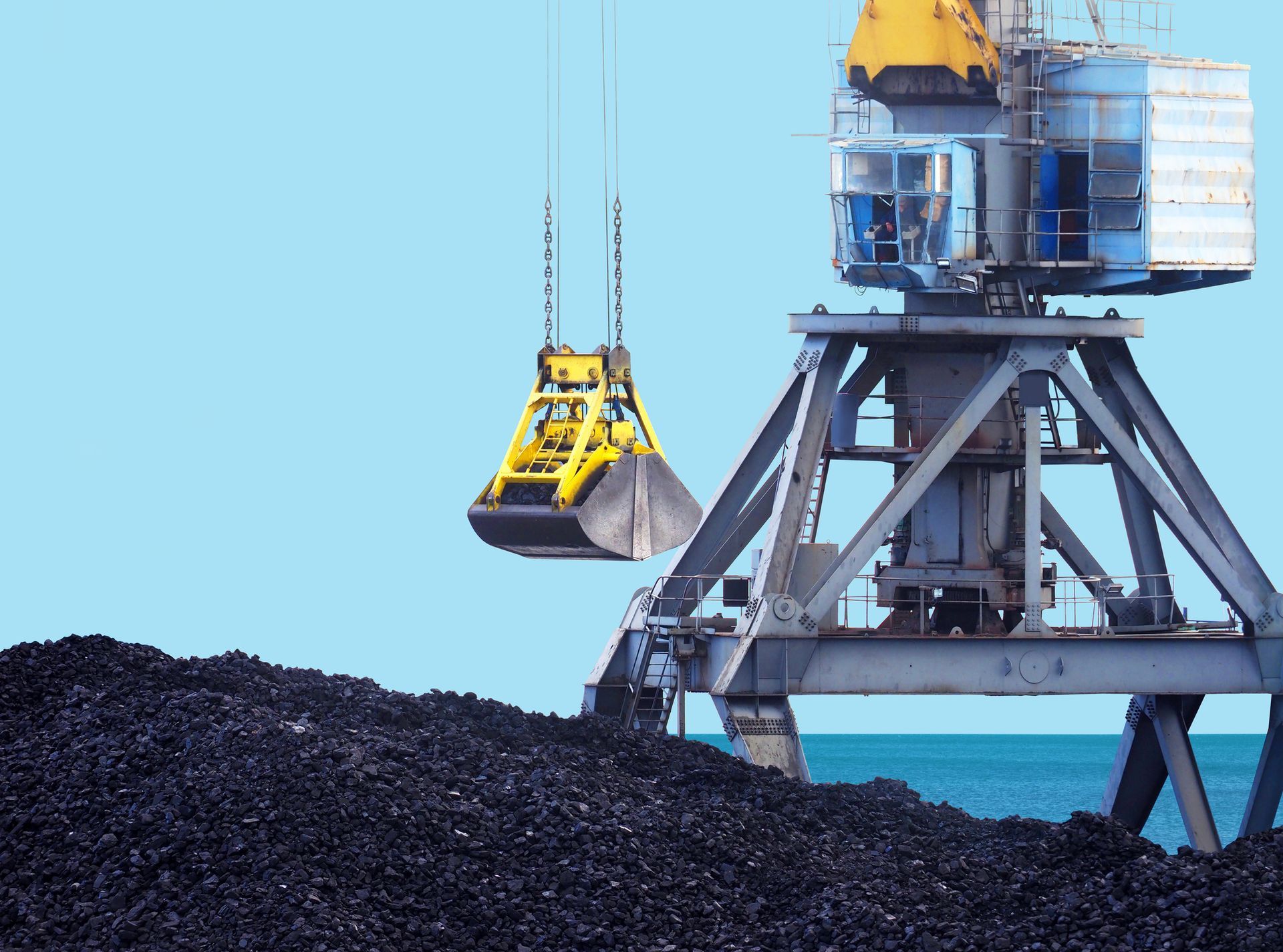 A crane is lifting a large pile of coal into the ocean