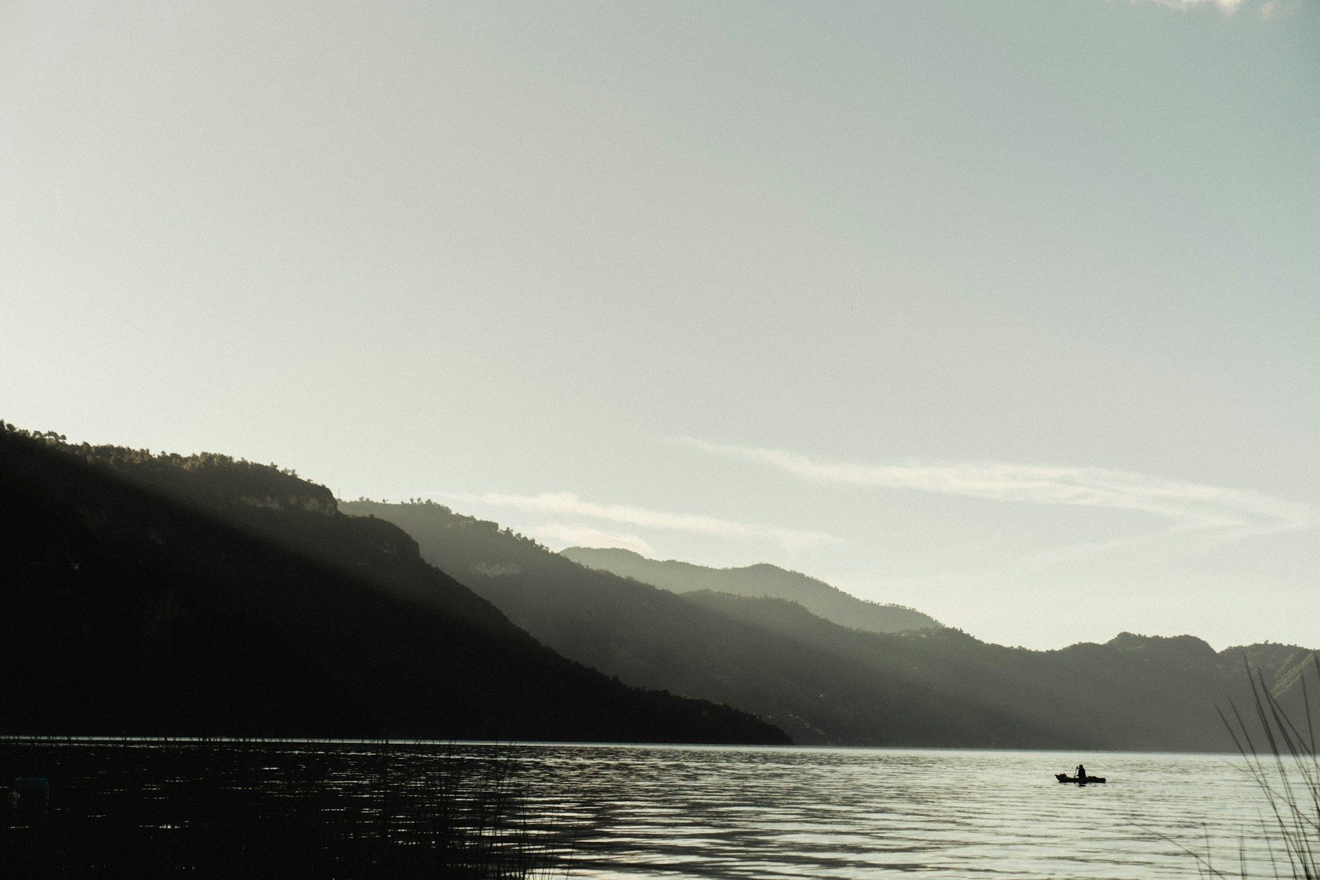 Una persona está haciendo kayak en un lago con montañas al fondo.