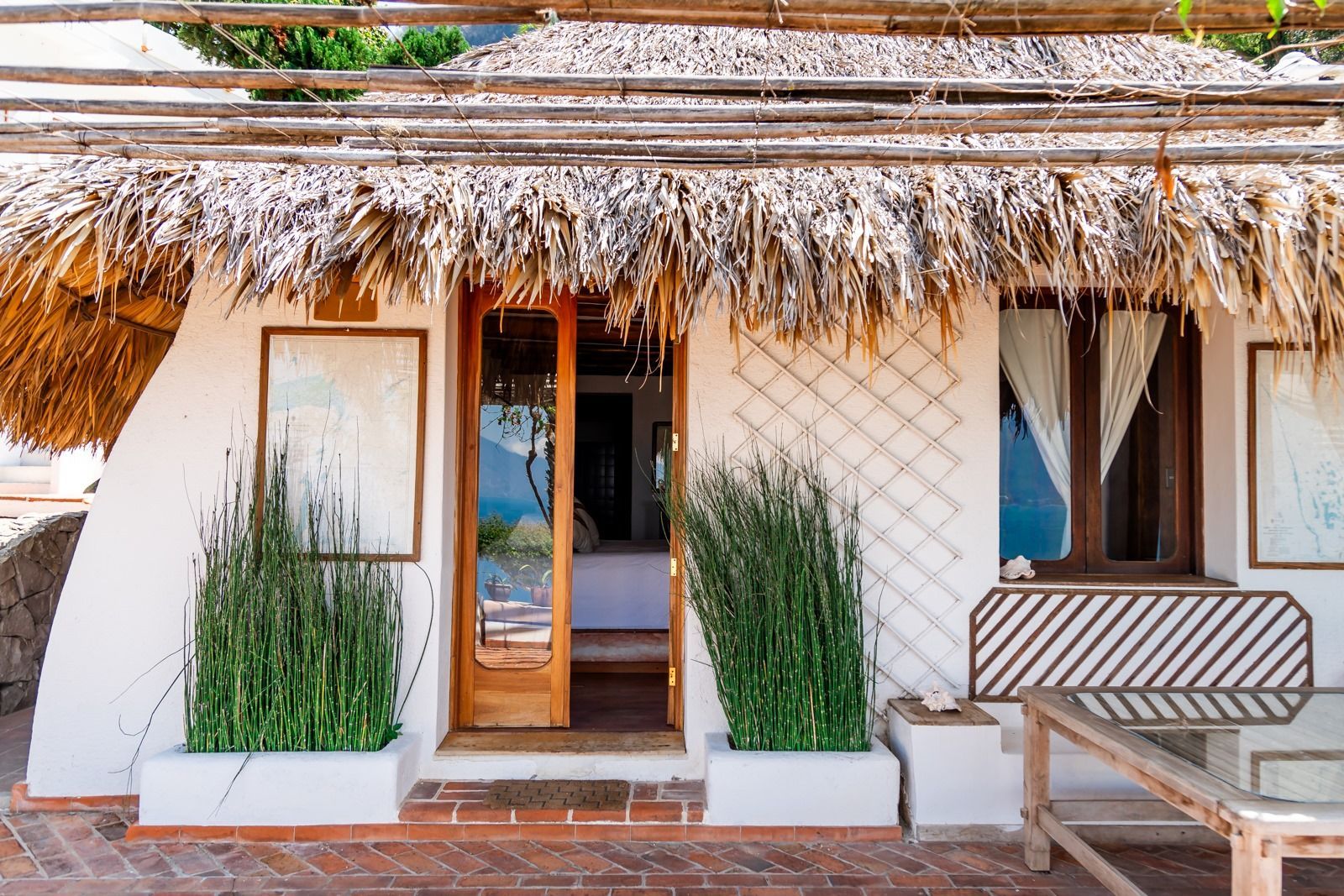 Una casa blanca con techo de paja y un banco delante de ella. Tzampoc Resort