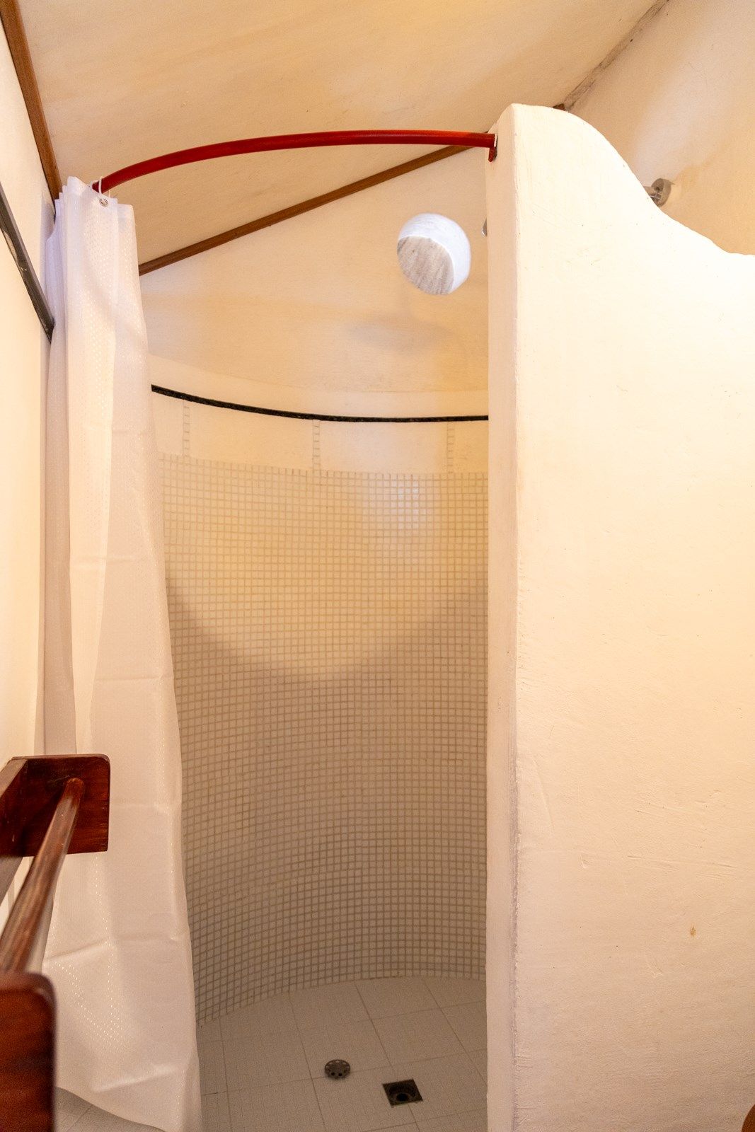 Una ducha con cortina blanca y barandilla roja.