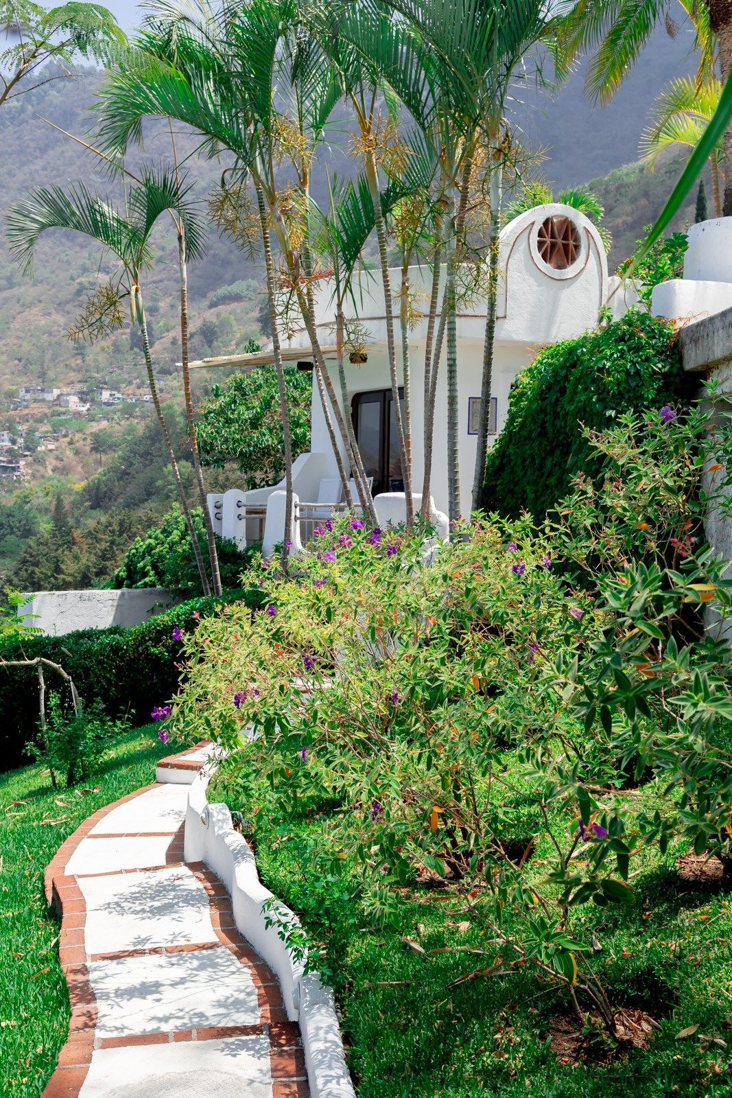 Una pasarela que conduce a una casa blanca rodeada de árboles y arbustos. Tzampoc Resort