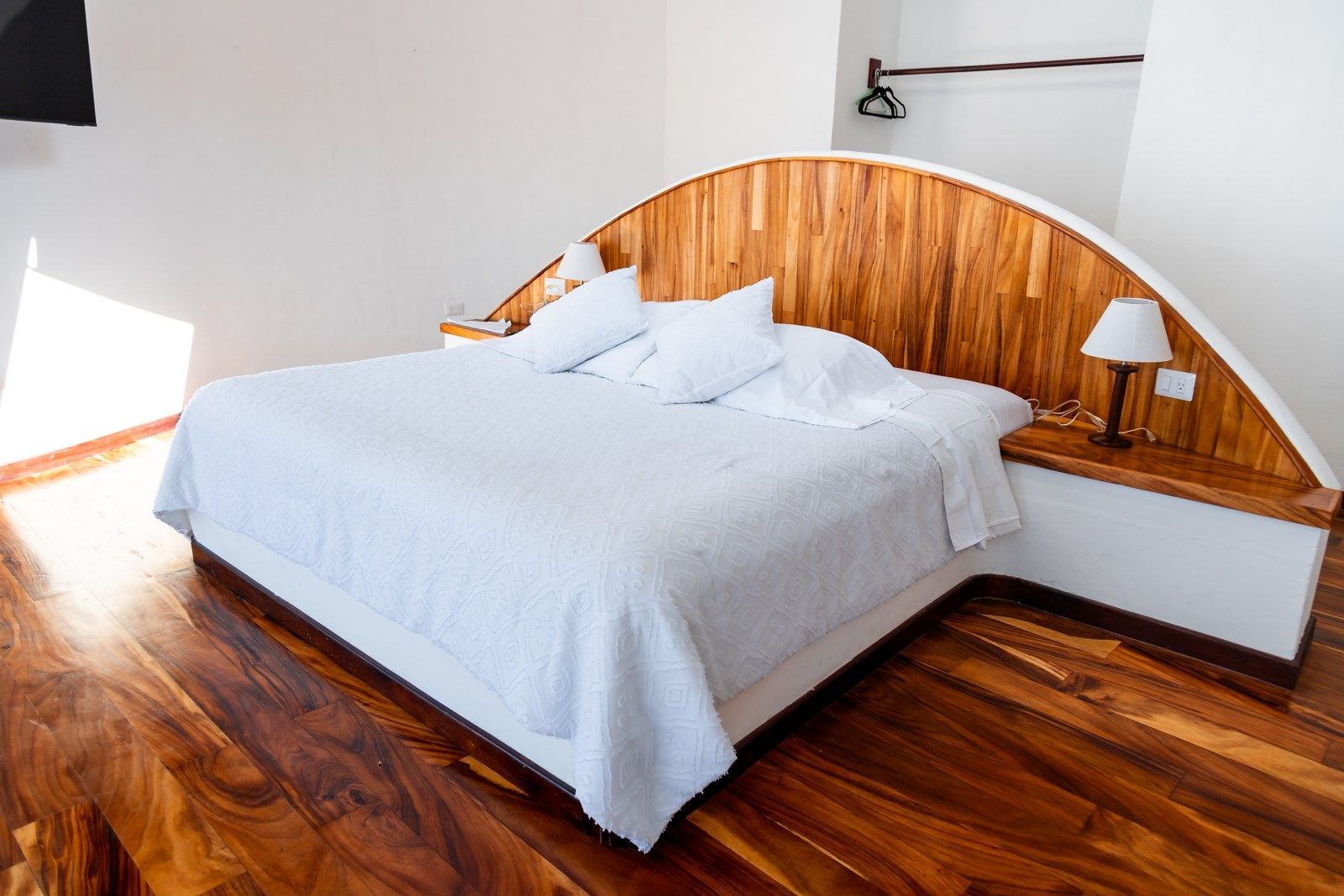 Una cama con sábanas blancas y un cabecero de madera en una habitación de hotel.