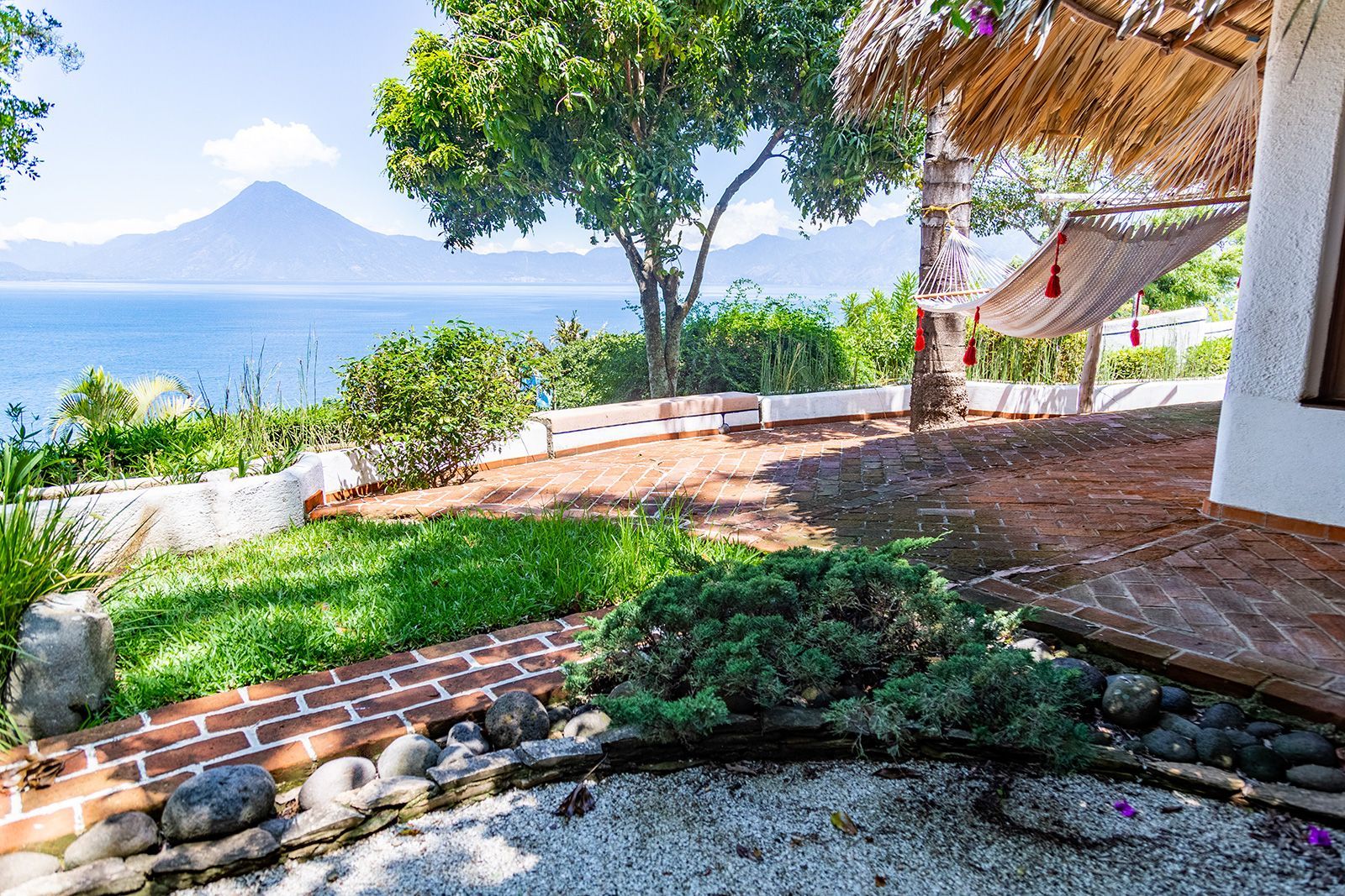 Una hamaca cuelga de un árbol frente a una casa con vista al océano.