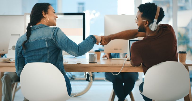 A man and a woman are encouraging each other while sitting at a desk.