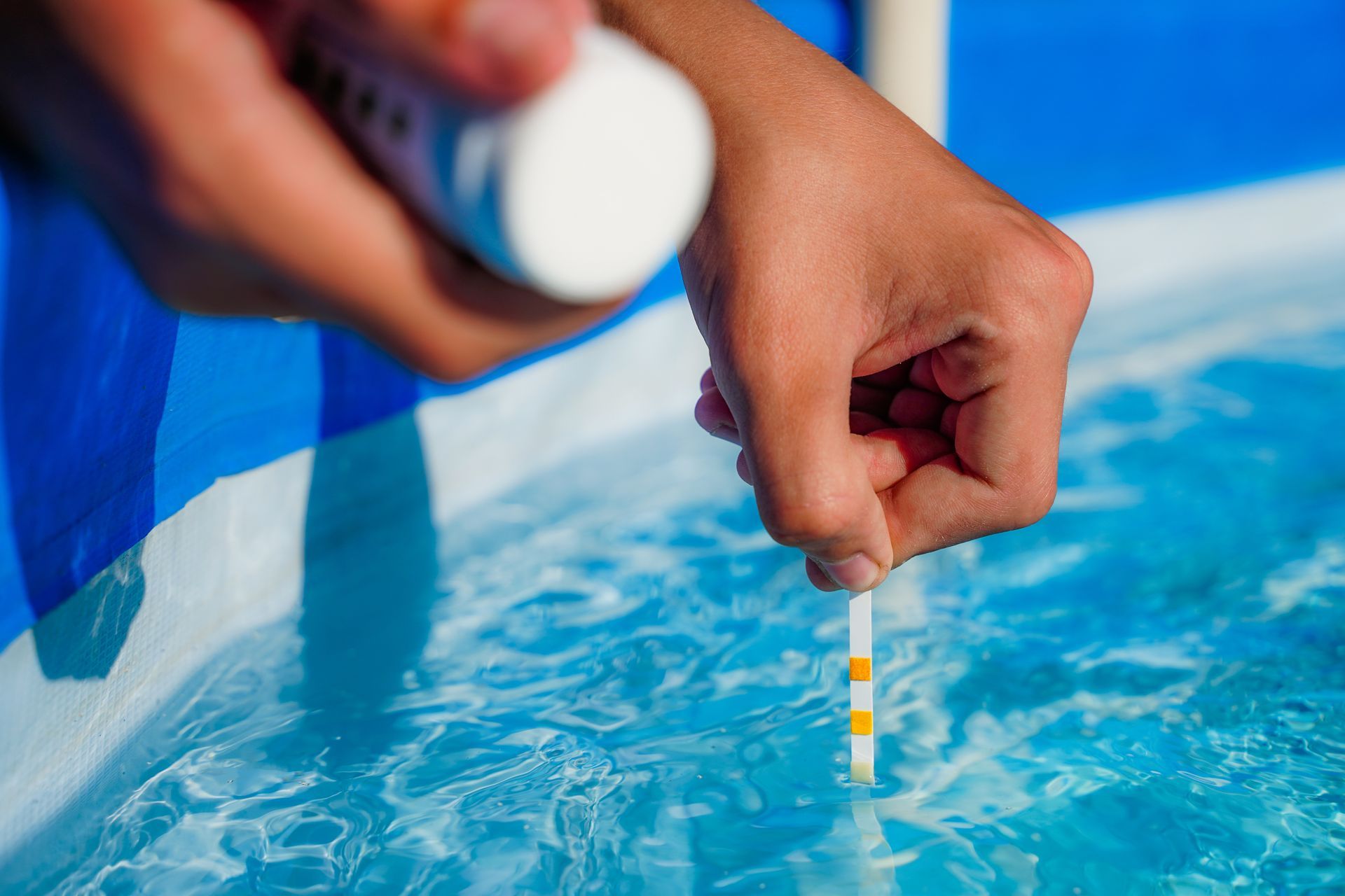 A person is measuring the ph of a swimming pool with a test strip.