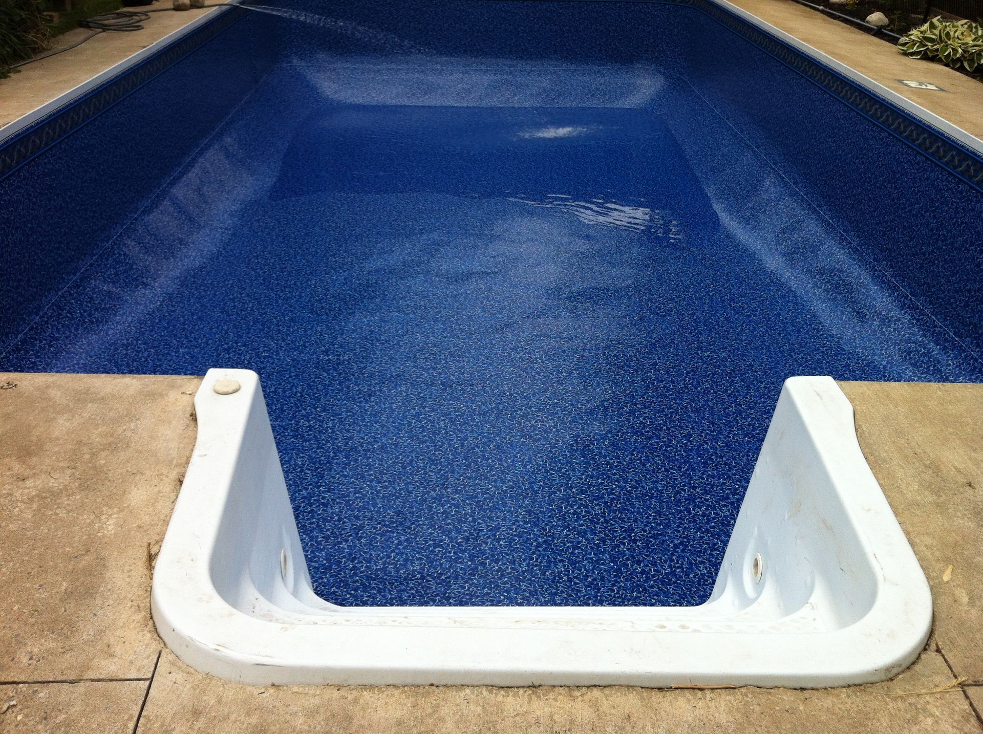 A blue swimming pool with a white staircase leading to it