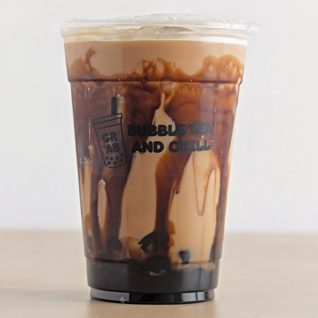 Iced brown sugar bubble tea with dark drips in a clear plastic cup.