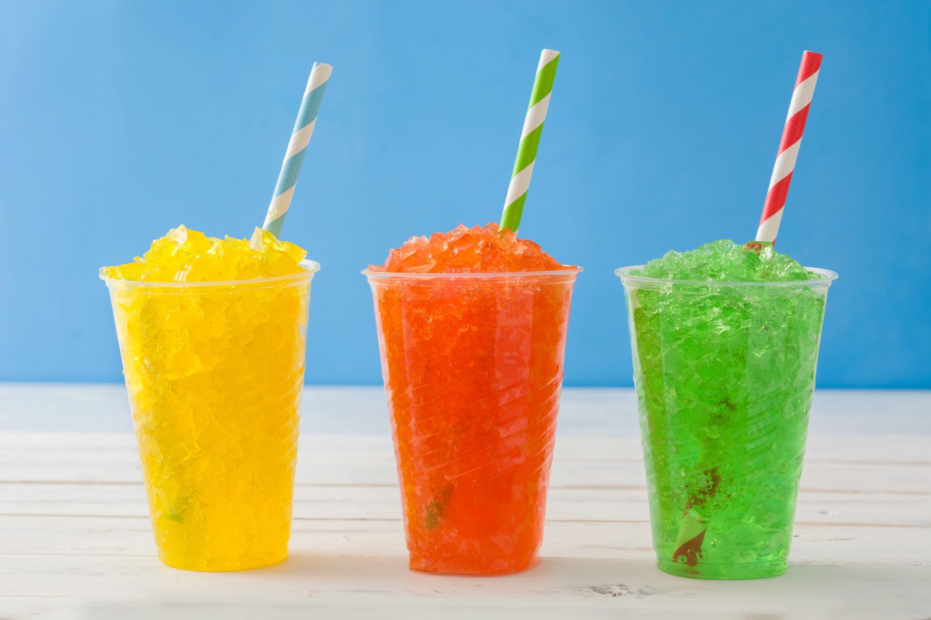 Three colorful slushies with striped straws against a blue background.