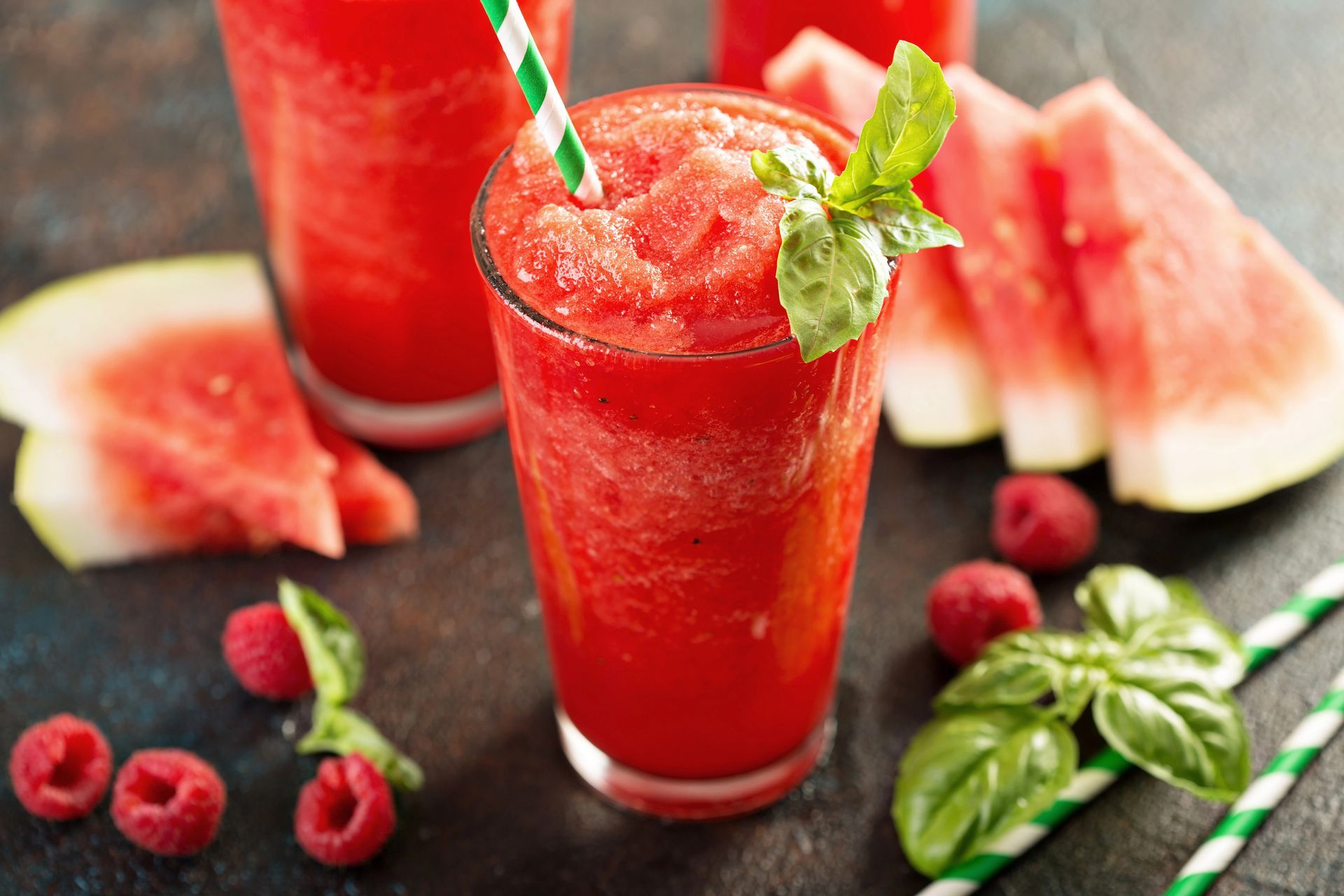 Watermelon smoothie in glasses with fruit slices and basil garnish.