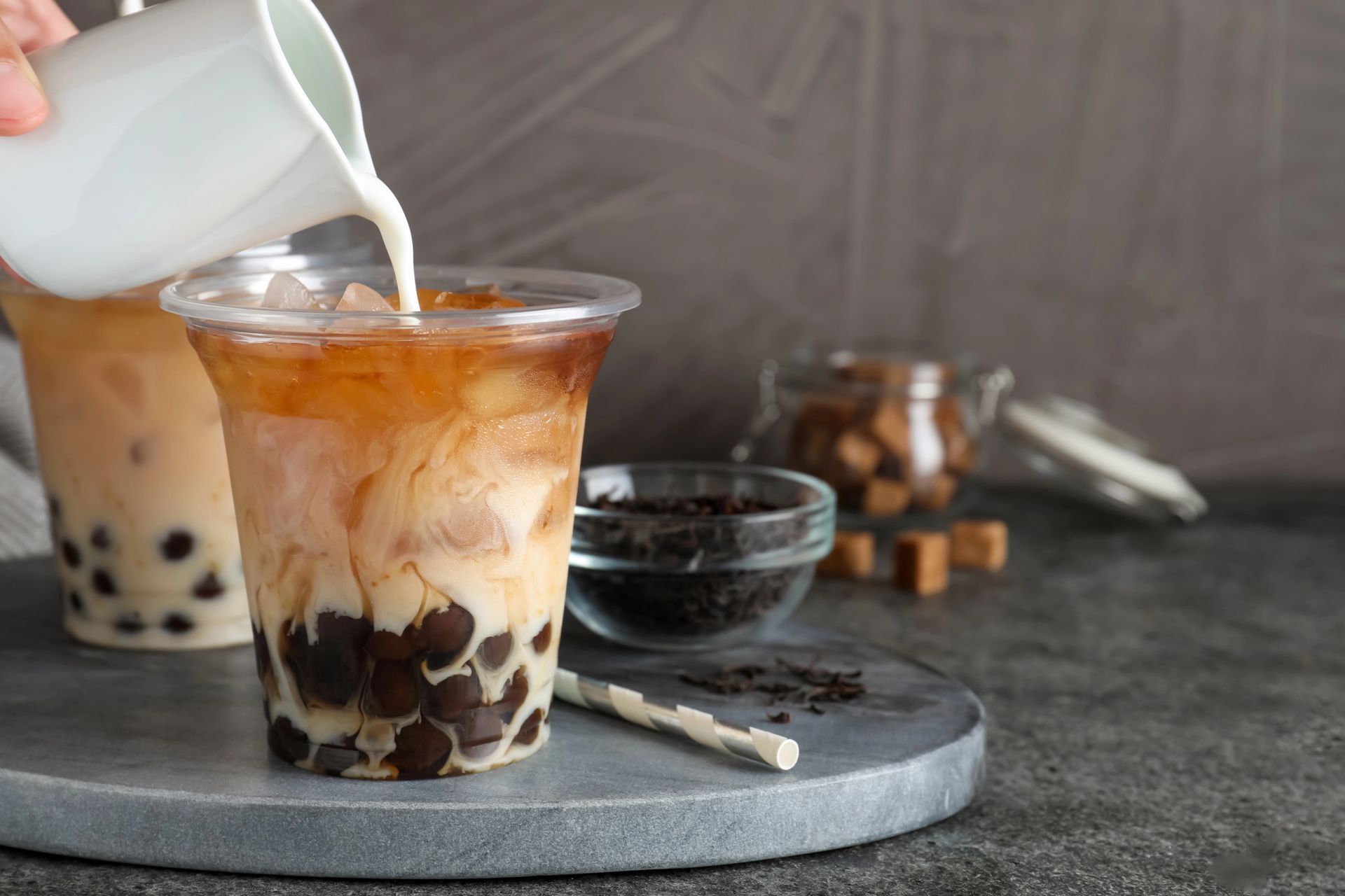 Milk being poured into a bubble tea with tapioca pearls, brown sugar, and tea leaves.