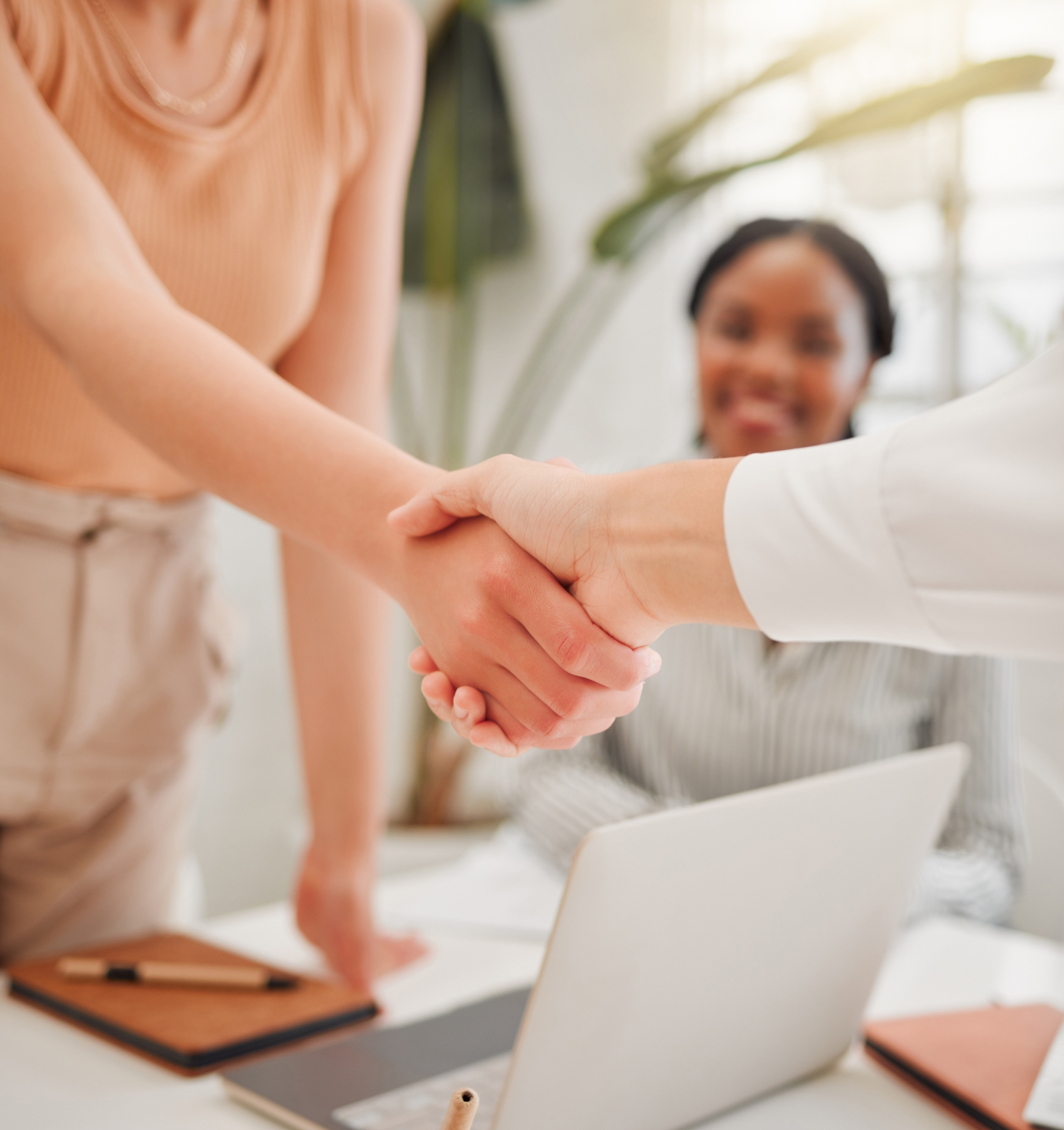 A man and a woman are shaking hands in front of a laptop.