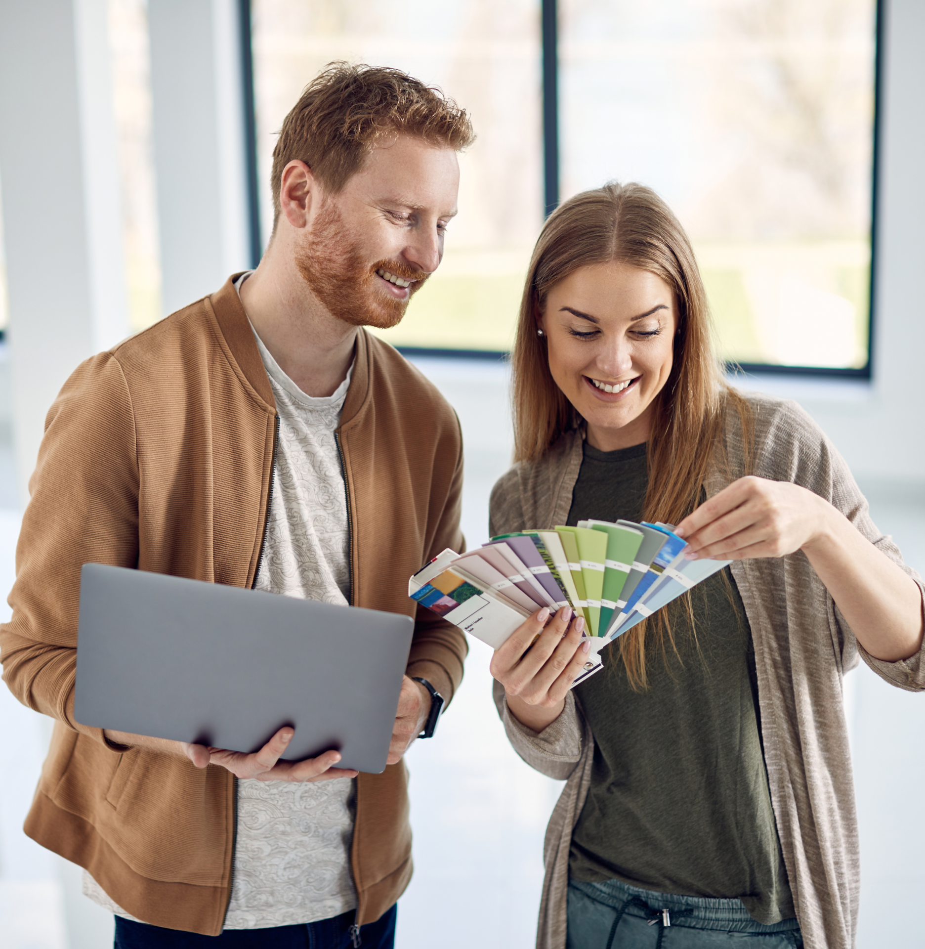 A man and a woman are looking at a color palette and a laptop.