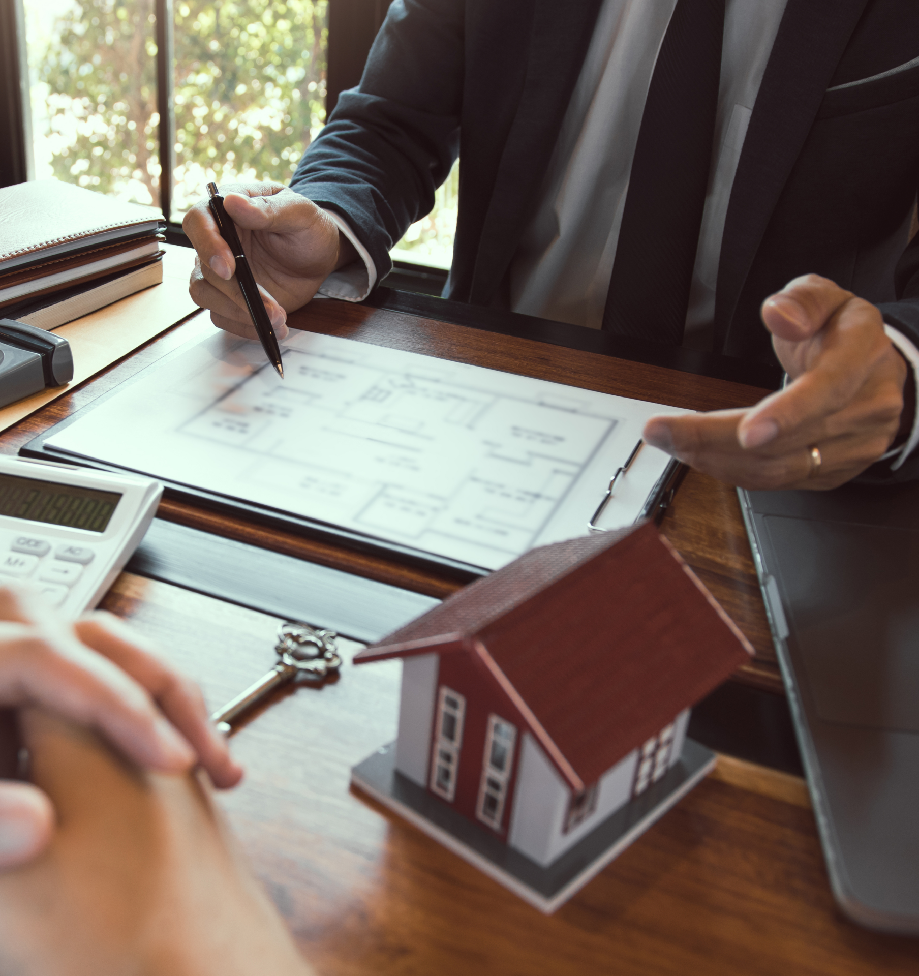 A man is sitting at a desk with a model house and a calculator