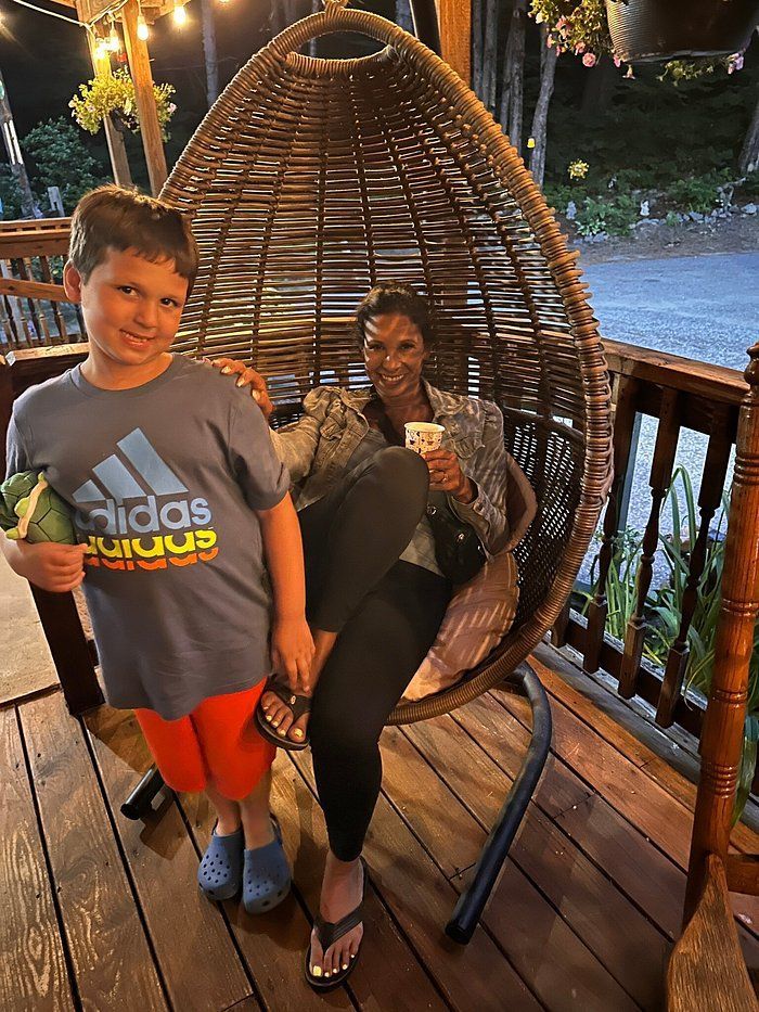 A woman and a boy are sitting in a wicker chair on a deck.