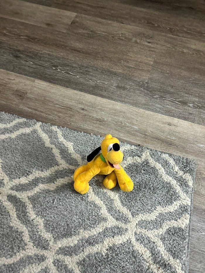 A stuffed dog is sitting on a rug on the floor.