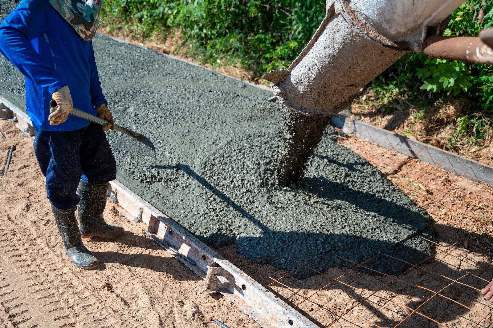 Construction worker pouring concrete into a sidewalk form.
