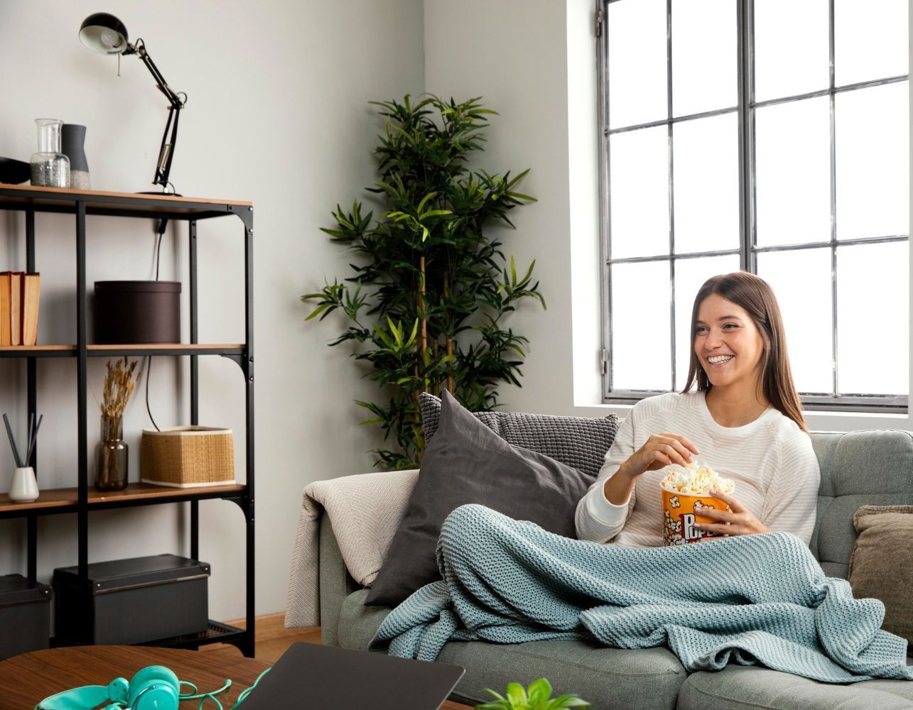 A woman is sitting on a couch eating popcorn.