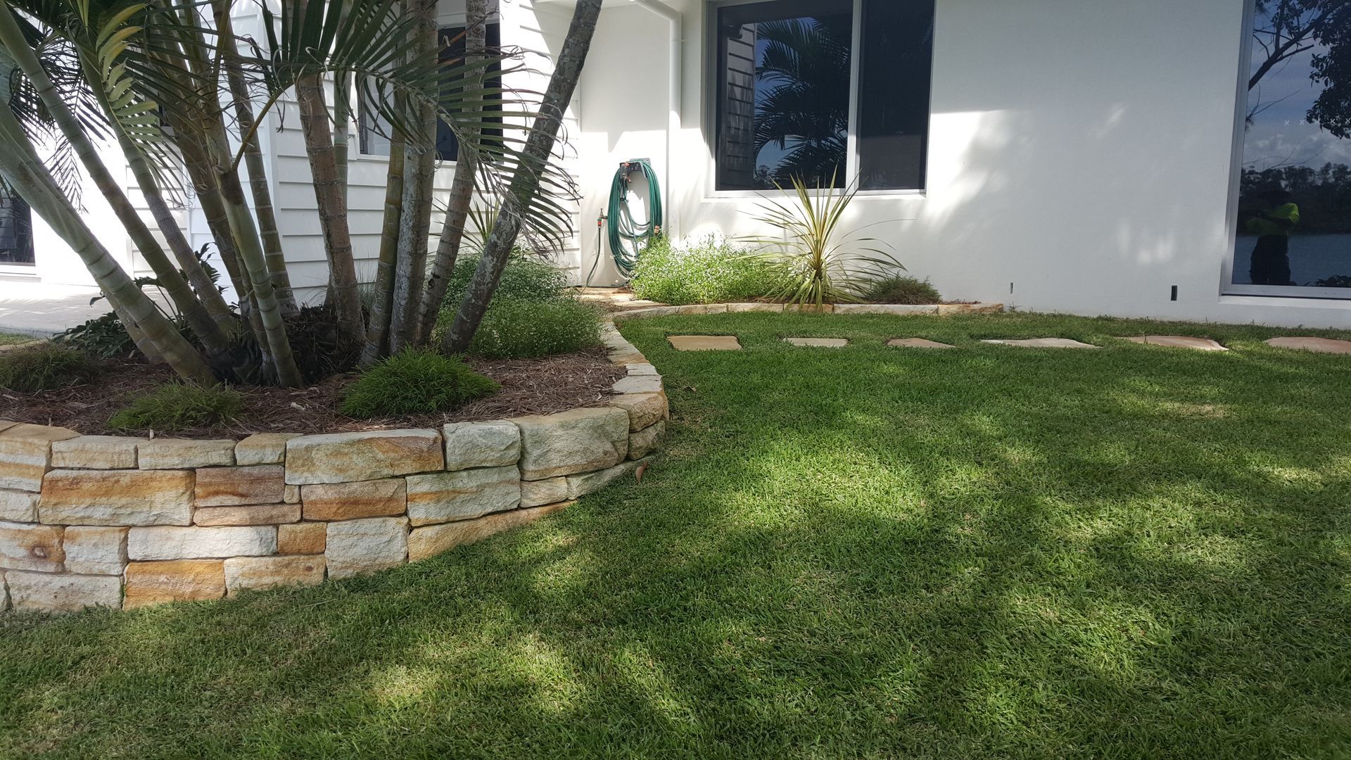 A retaining wall in a back lawn with pebbles and trees — Tim Williams Landscapes in Byron, NSW