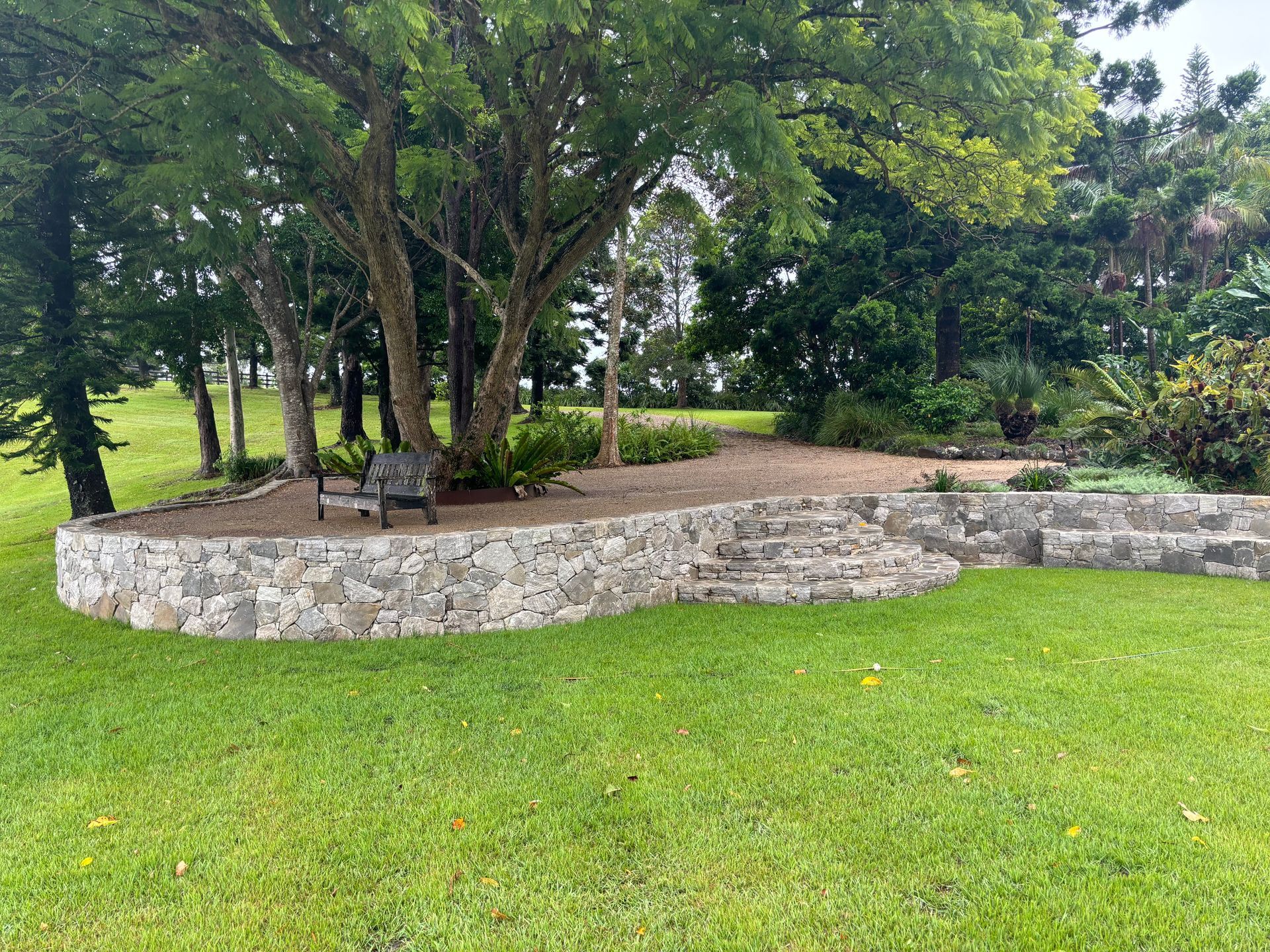 A retaining wall with steps leading up to a seat surrounded by trees — Tim Williams Landscapes in Lennox Head, NSW