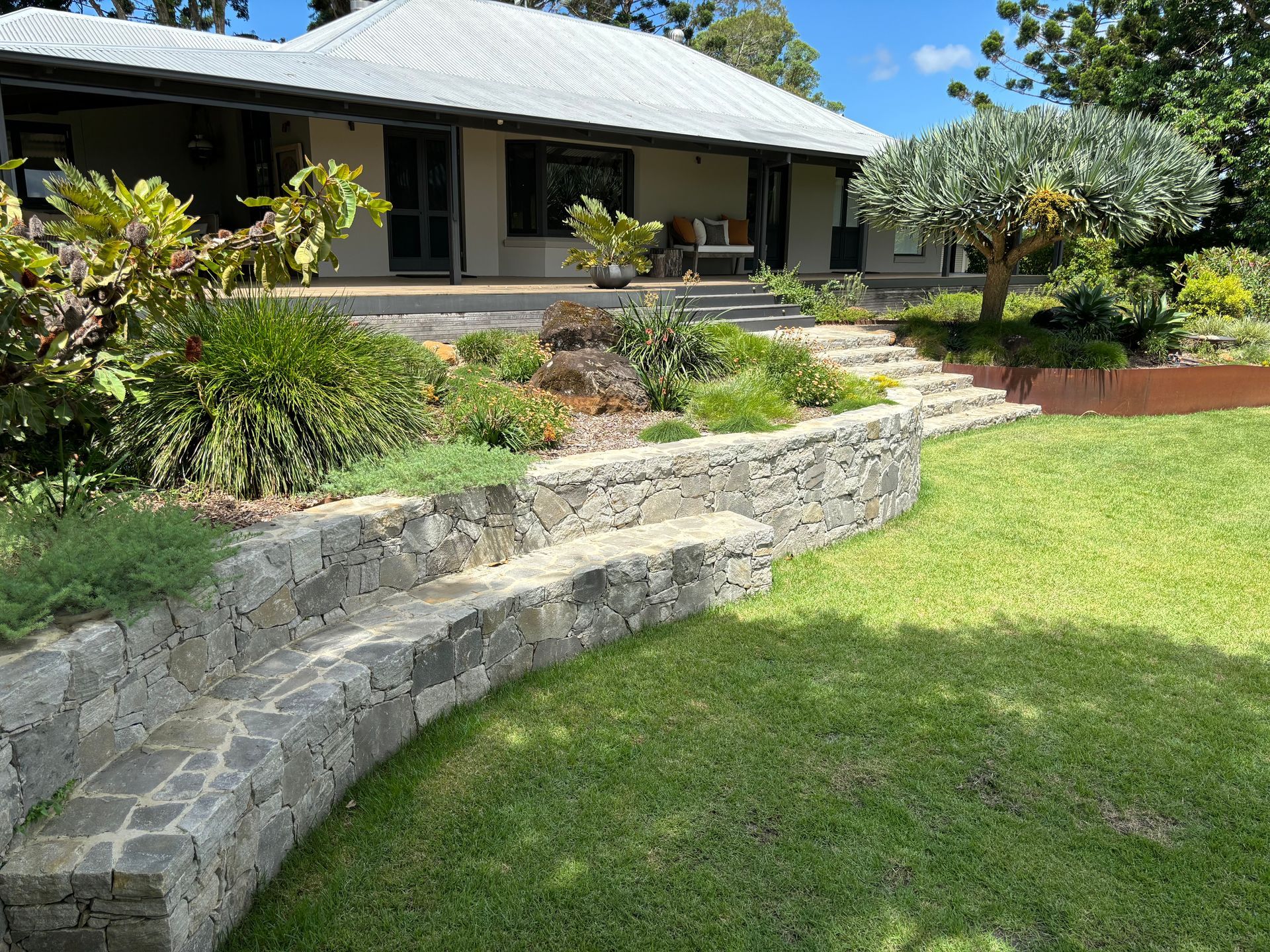 A garden and retaining wall leading up to a large house — Tim Williams Landscapes in Wollongbar, NSW
