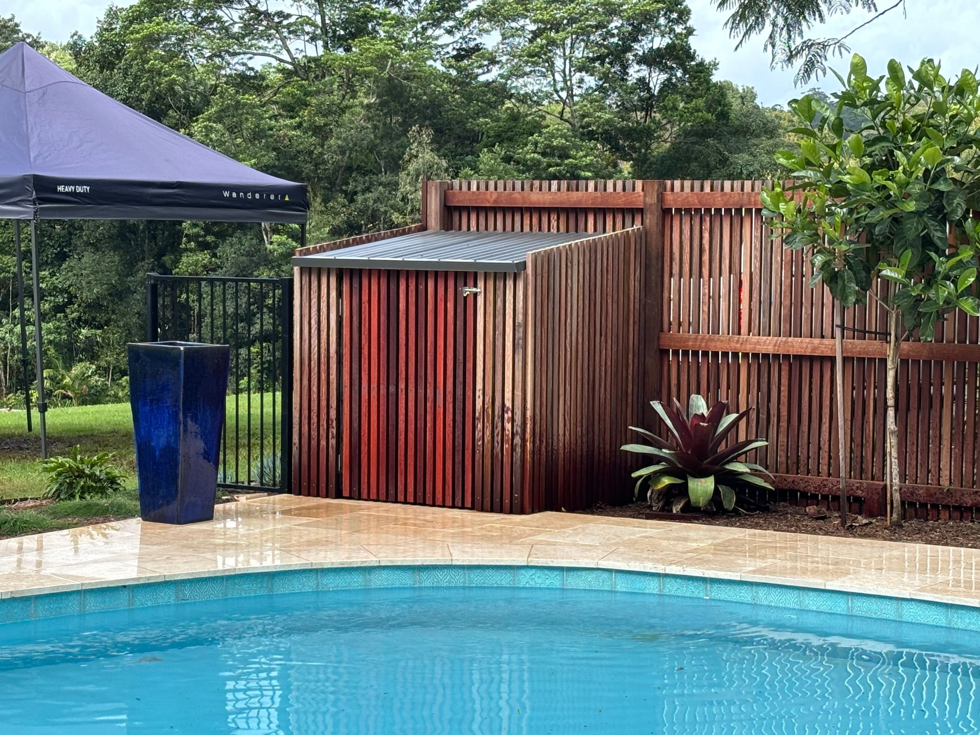 Poolside shed with wooden fence, blue vase, and a purple awning.