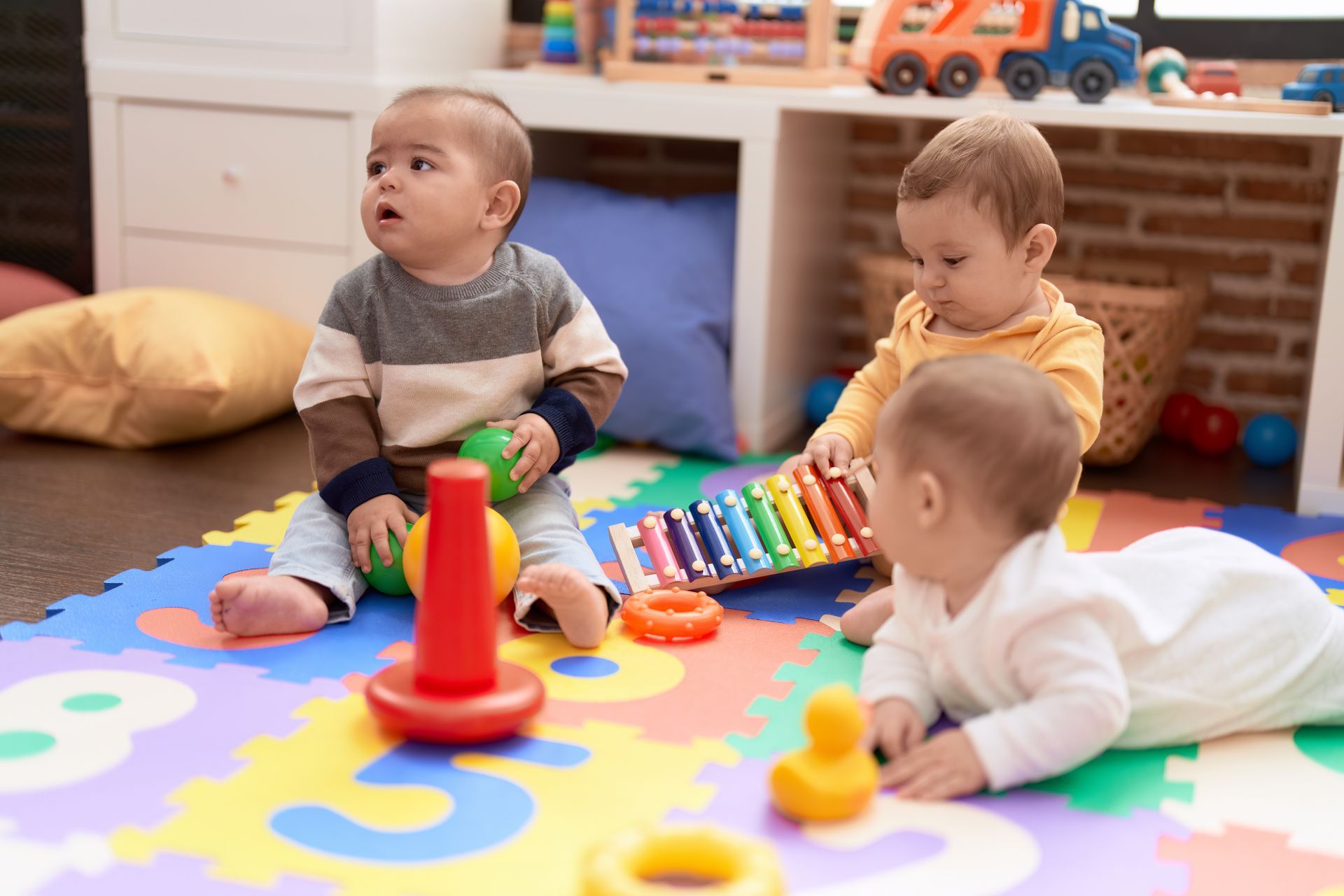 Three babies playing with toys on a colorful play mat.