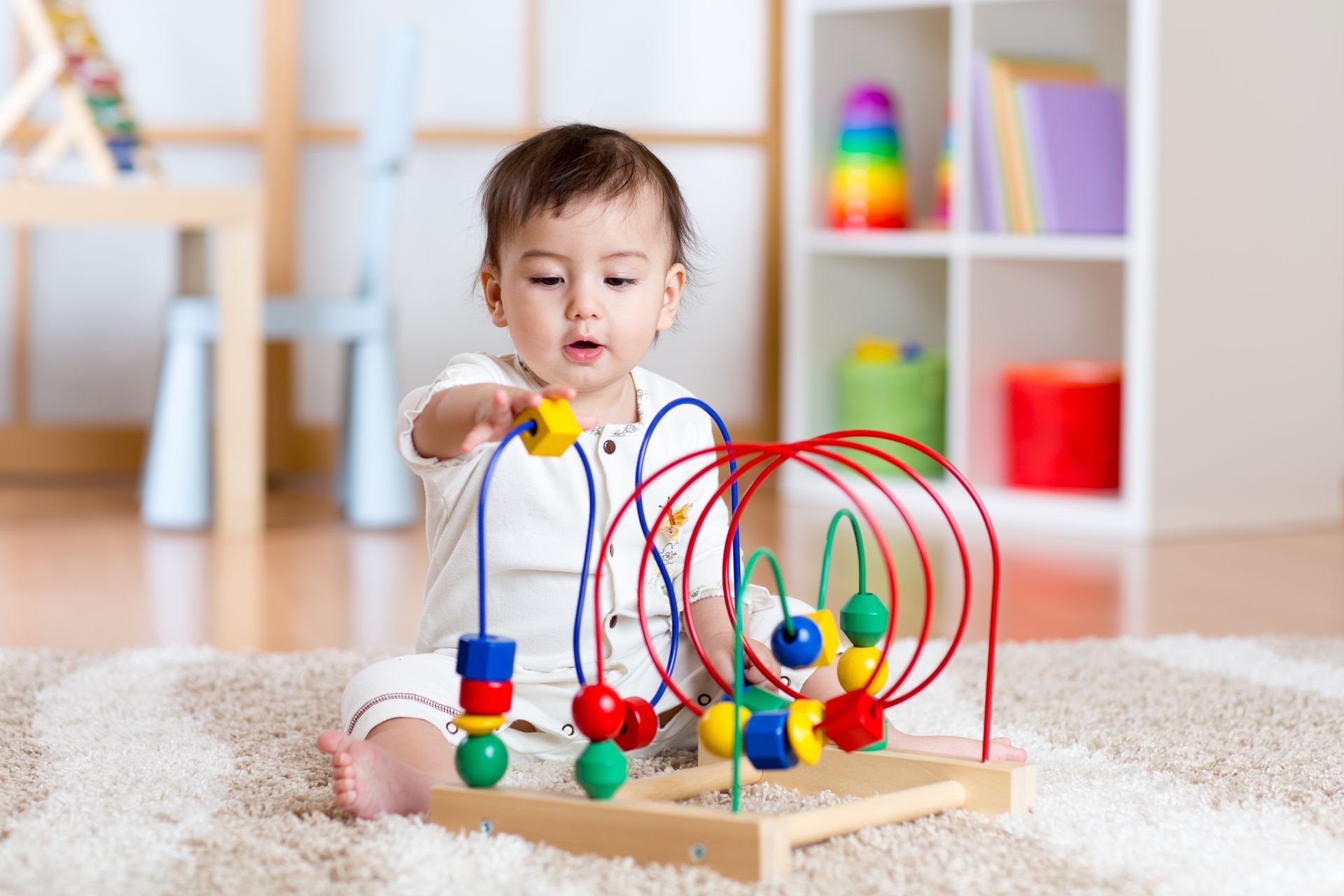 Baby playing with a colorful bead maze on a carpeted floor.