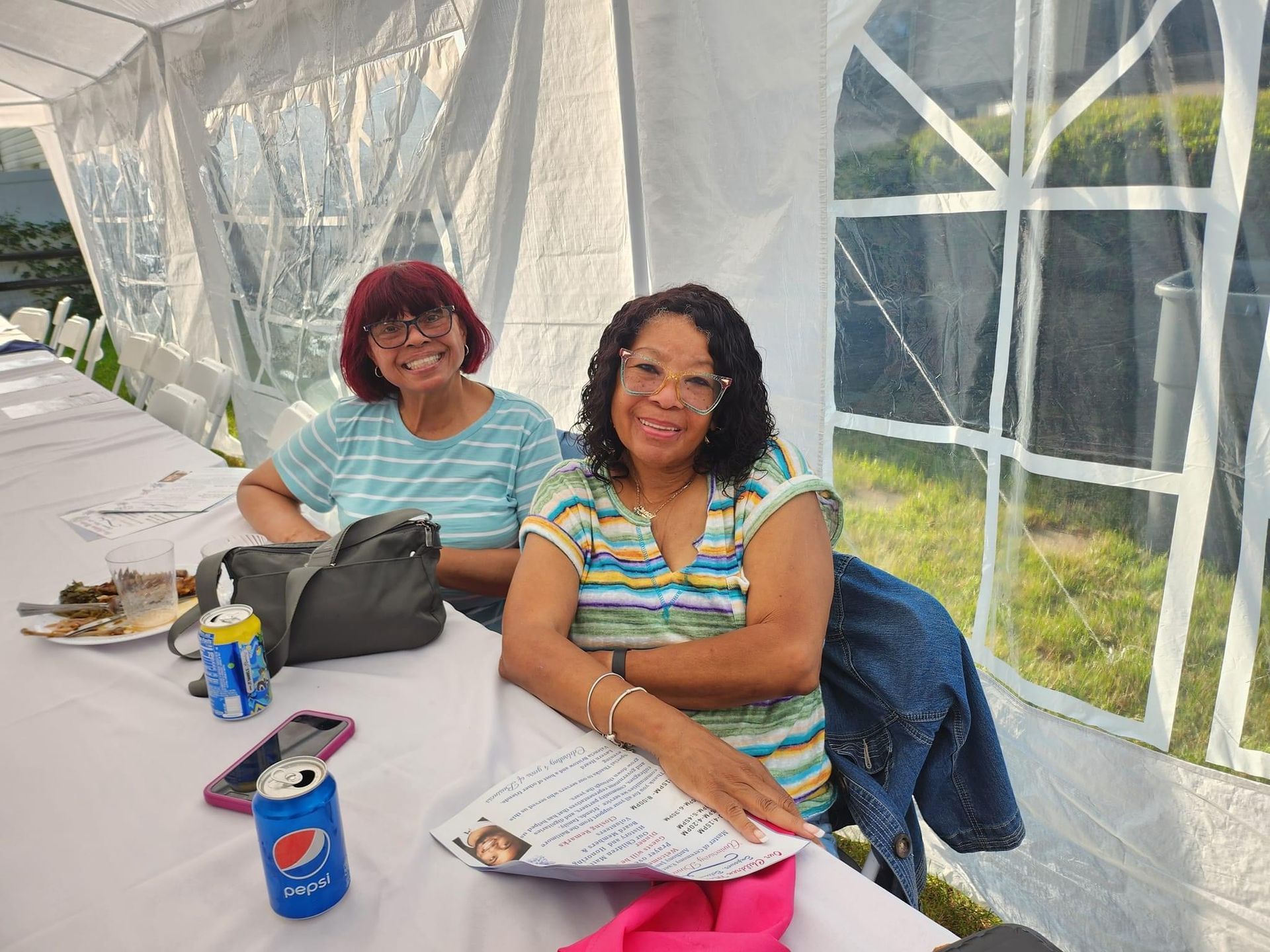 Two women are sitting at a table under a tent.