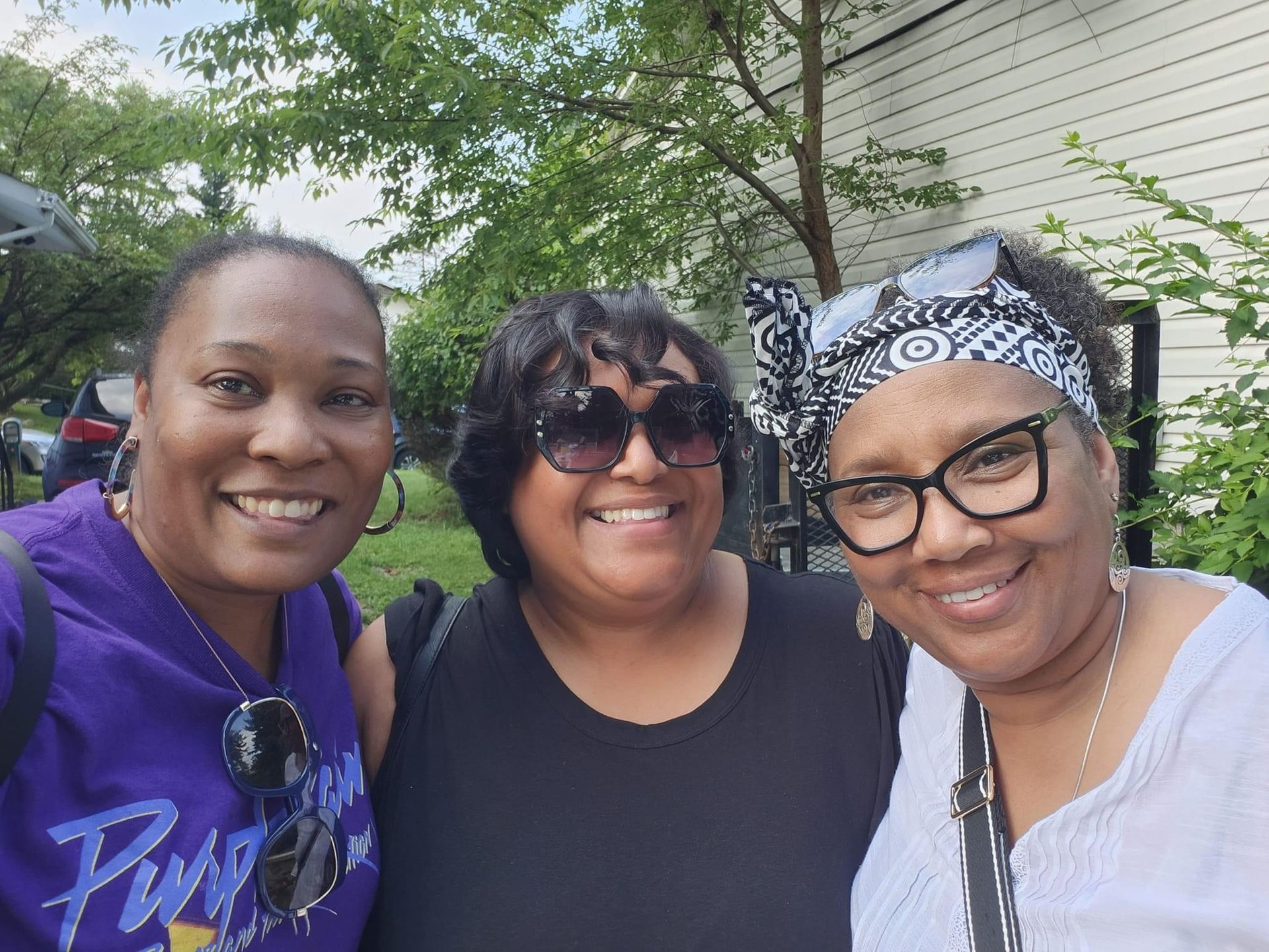 Three women are posing for a picture in front of a house.