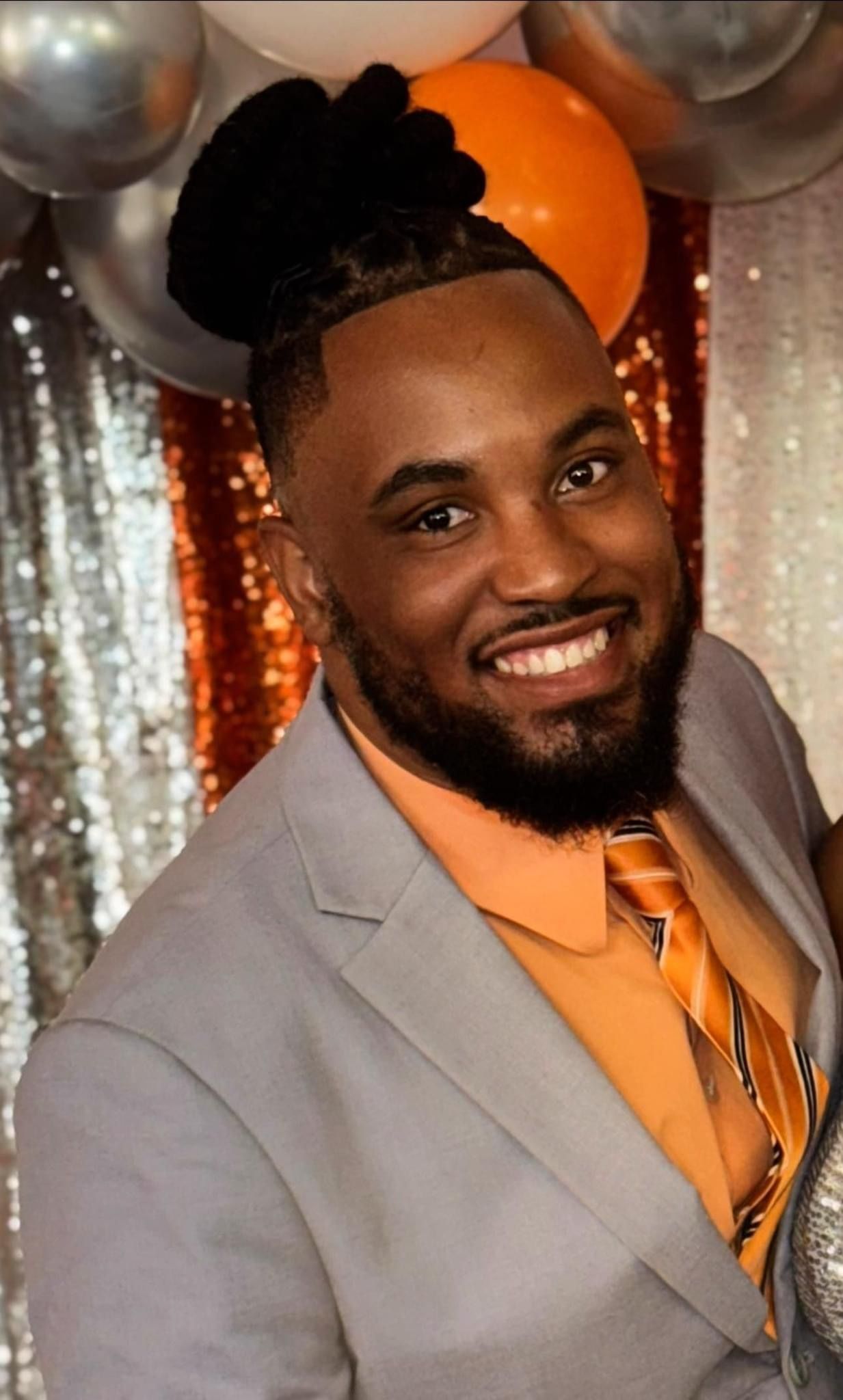 A man in a suit and tie is smiling in front of balloons.