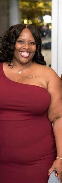 A woman is wearing a red one shoulder dress and smiling.