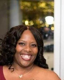 A woman in a red dress is smiling and wearing a necklace.