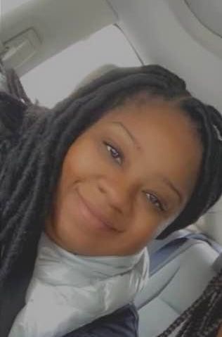 A woman with braids is smiling while sitting in the back seat of a car.