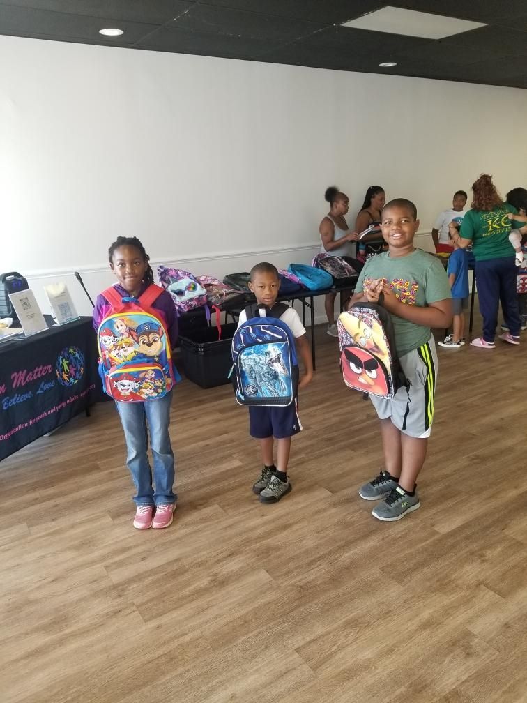 Three children are standing next to each other in a room holding backpacks.